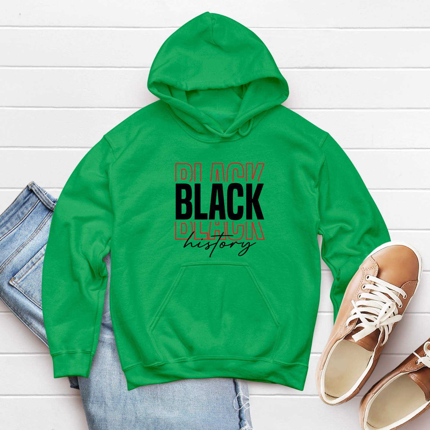 Green hoodie with 'Black History' text on a white wooden surface with jeans and shoes.