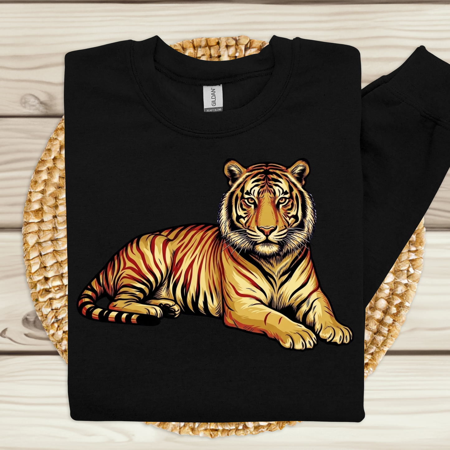 A black crewneck sweatshirt featuring a detailed graphic of a tiger lying down, displayed on a woven mat over a light wood background.