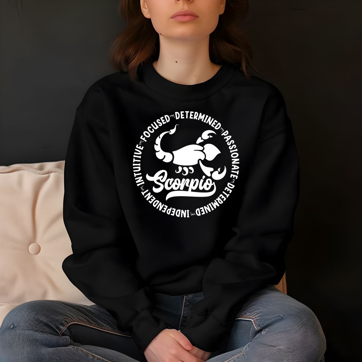Woman wearing a black crewneck sweatshirt featuring a white circular Scorpio zodiac graphic with a scorpion illustration, the word "Scorpio," and trait keywords like intuitive, focused, determined, passionate, and independent.