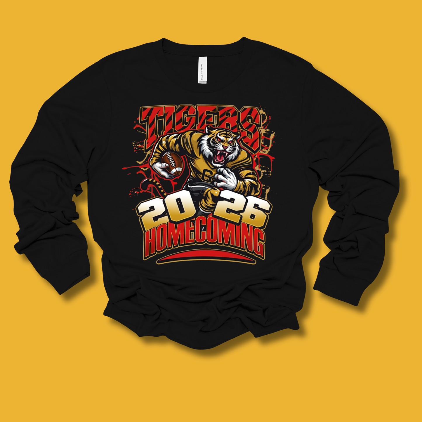 A black long-sleeve crewneck sweatshirt featuring a graphic print of a tiger holding a football, with the text 'TIGERS 2026 HOMECOMING' in red, yellow, and white. The sweatshirt is displayed flat against a solid mustard yellow background.