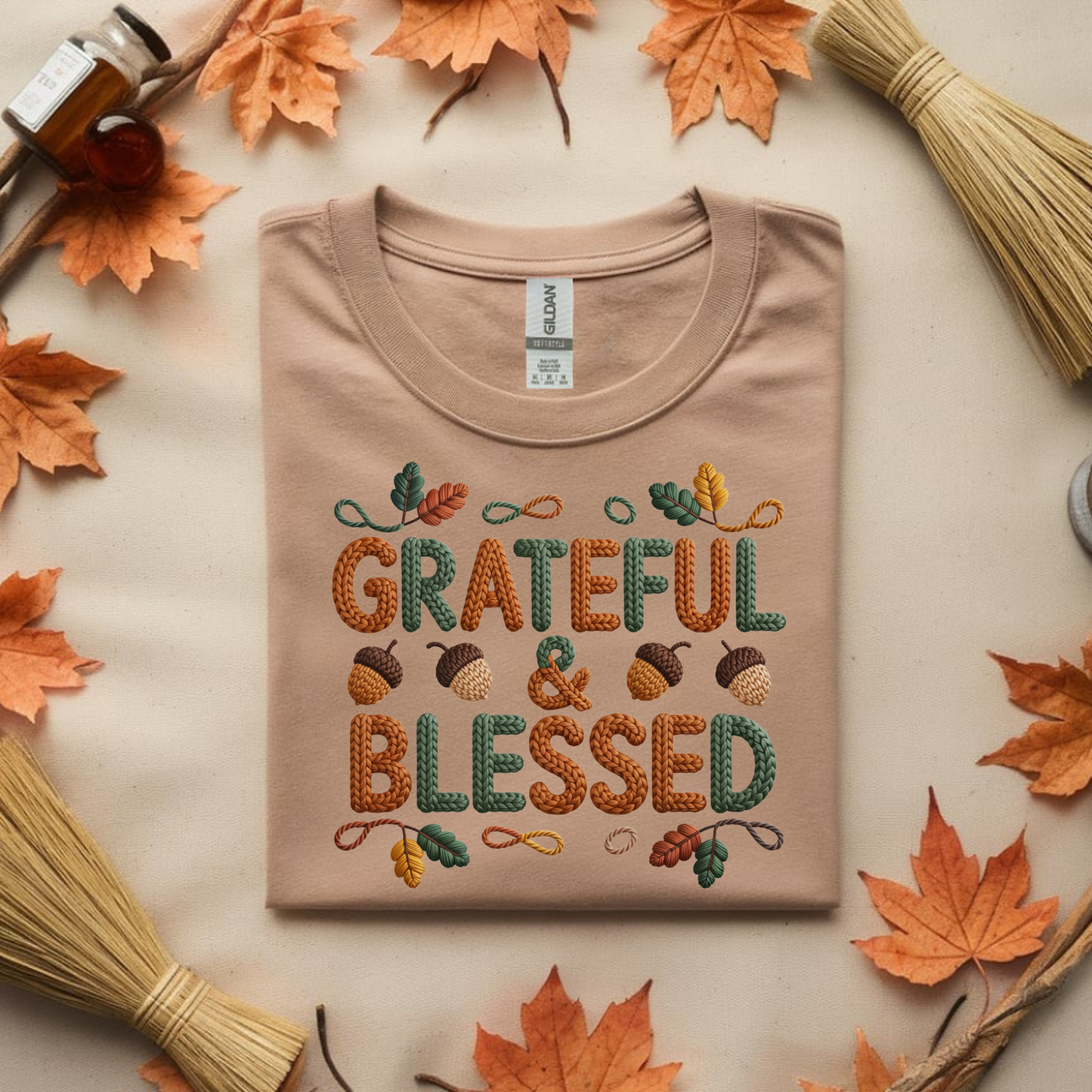 Beige t-shirt with 'GRATEFUL & BLESSED' text surrounded by autumn leaves and twigs on a beige background