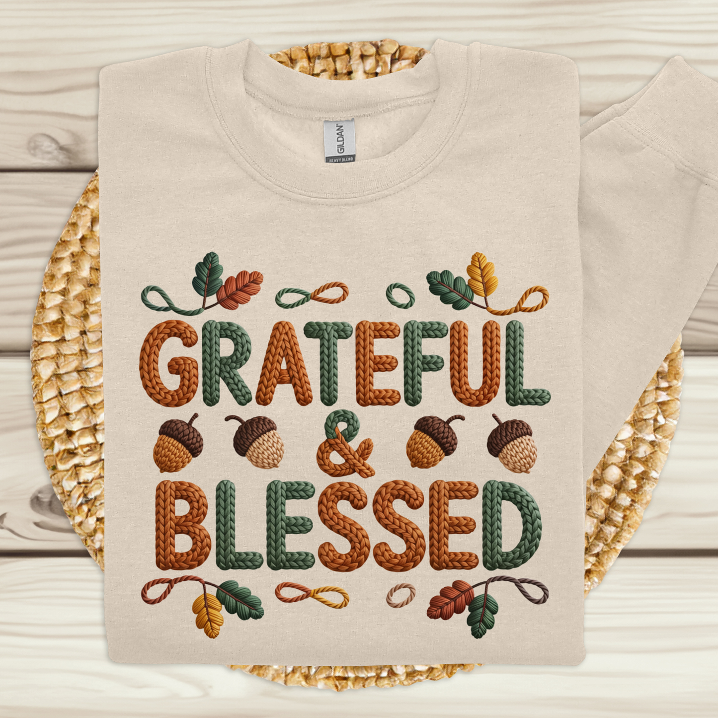 Beige sweatshirt with 'Grateful & Blessed' text and autumn-themed design on a woven mat.