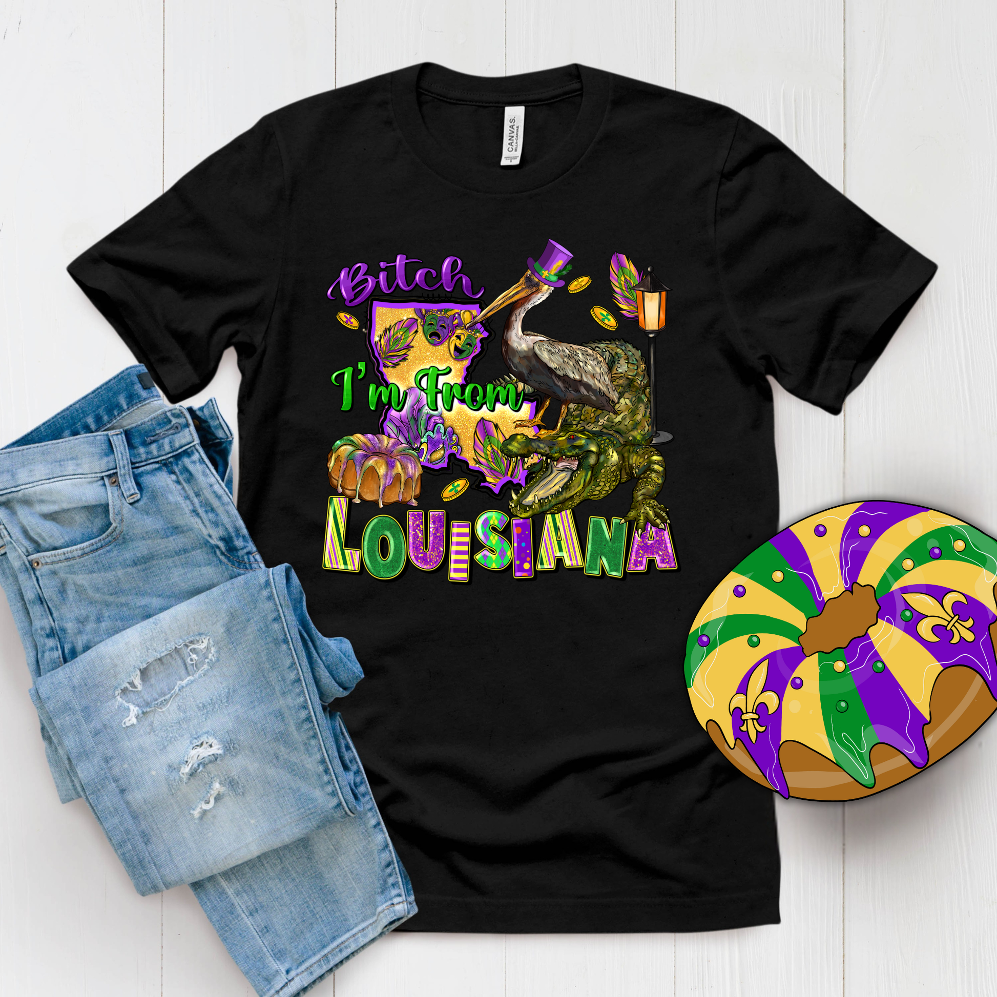 Black t-shirt with colorful text and graphics, paired with denim shorts and a Mardi Gras-themed donut on a white background.