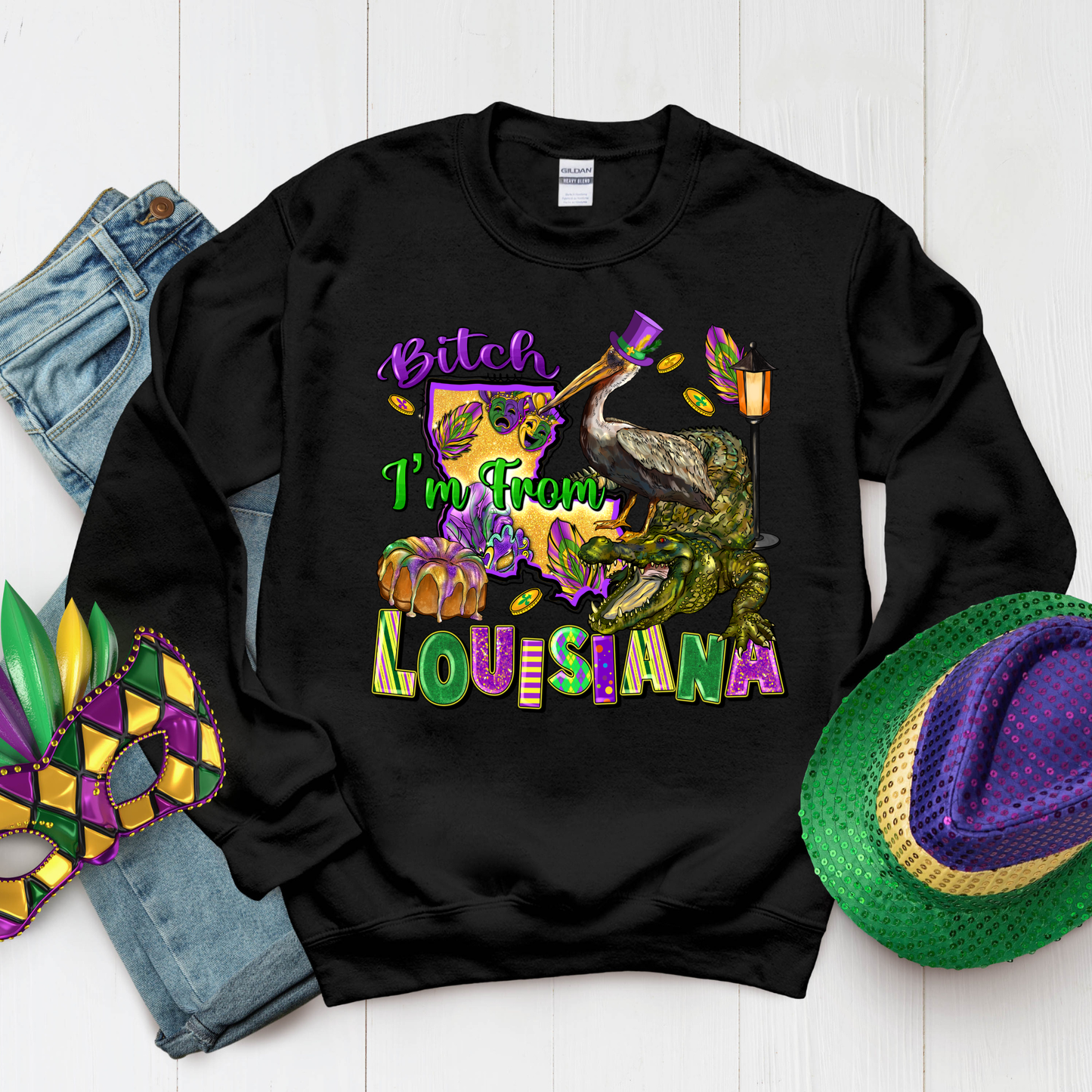 Black sweatshirt with colorful text and graphics, surrounded by Mardi Gras accessories on a white background.