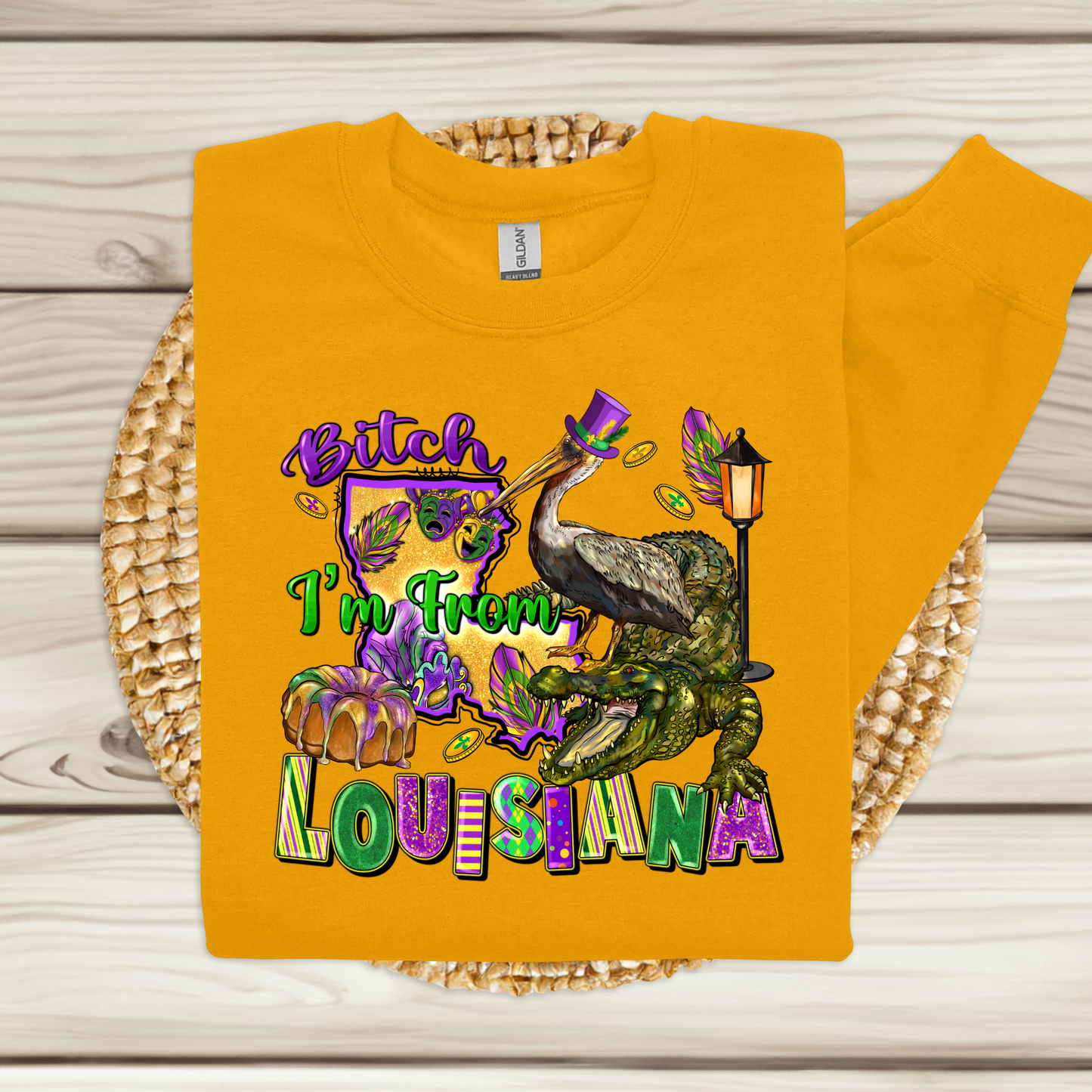 Yellow sweatshirt with colorful graphic and text 'Bitch I'm From Louisiana' on a woven mat.
