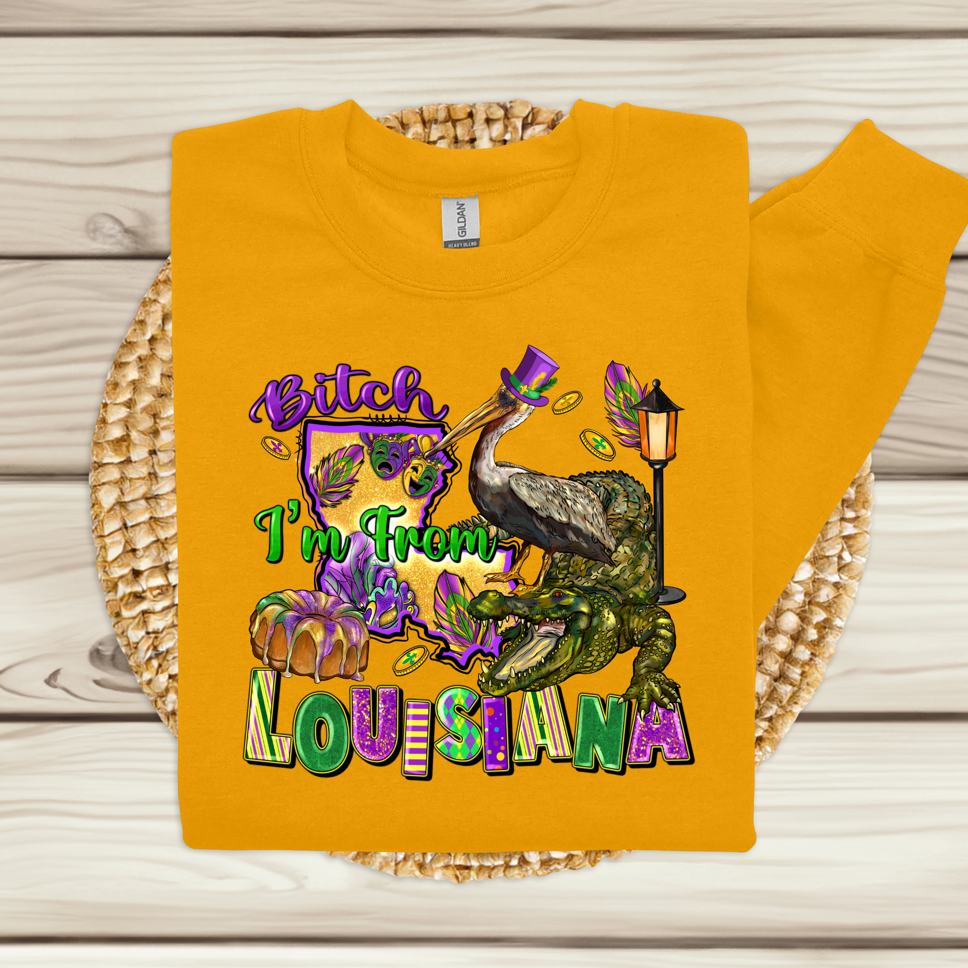 Yellow sweatshirt with colorful graphic and text 'Bitch I'm From Louisiana' on a woven mat.
