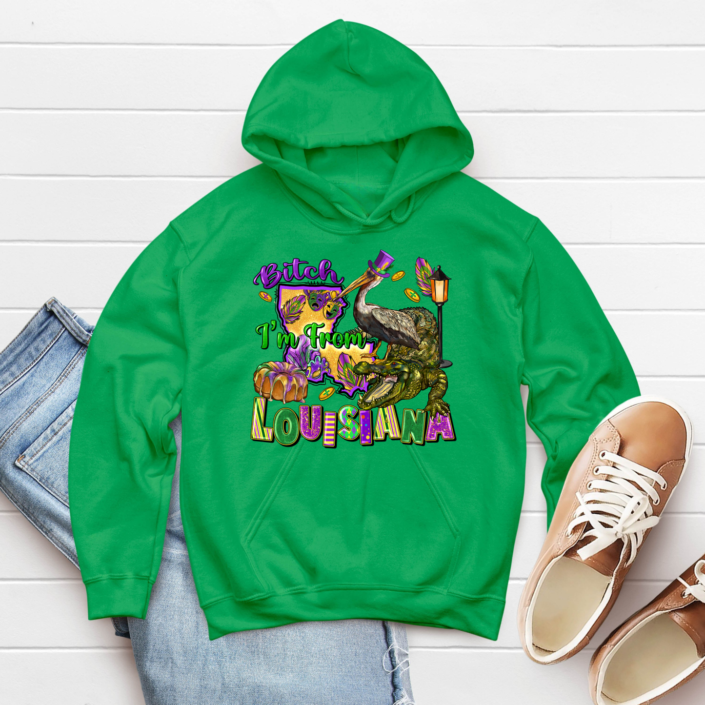 Green hoodie with 'I'm From Louisiana' graphic on a white wooden surface with jeans and shoes.