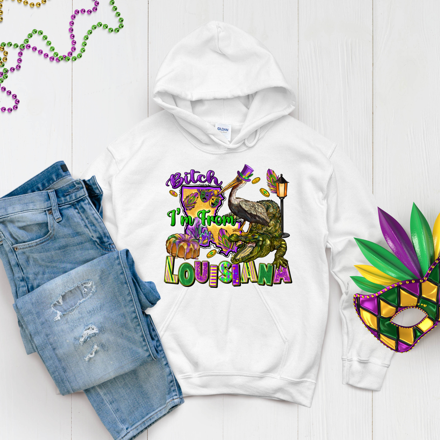 White hoodie with colorful graphic design, denim shorts, and Mardi Gras mask on a white background