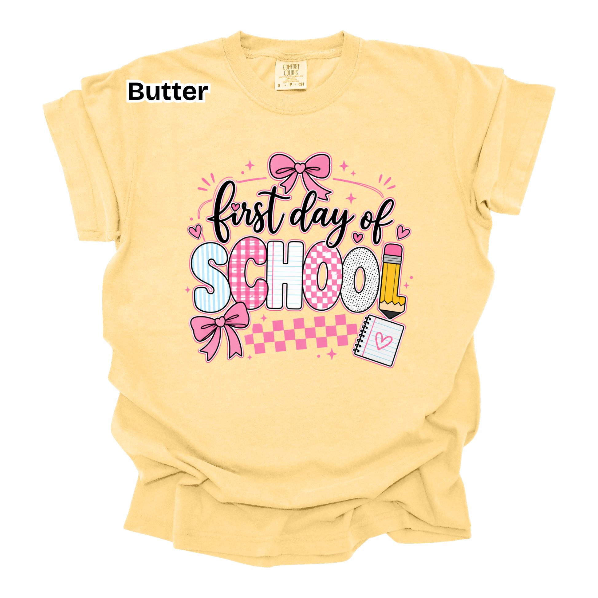 A pale butter-yellow short-sleeve t-shirt with a 'first day of SCHOOL' graphic on the front, featuring pink bows, a pencil, and a notepad, displayed on a white background.
