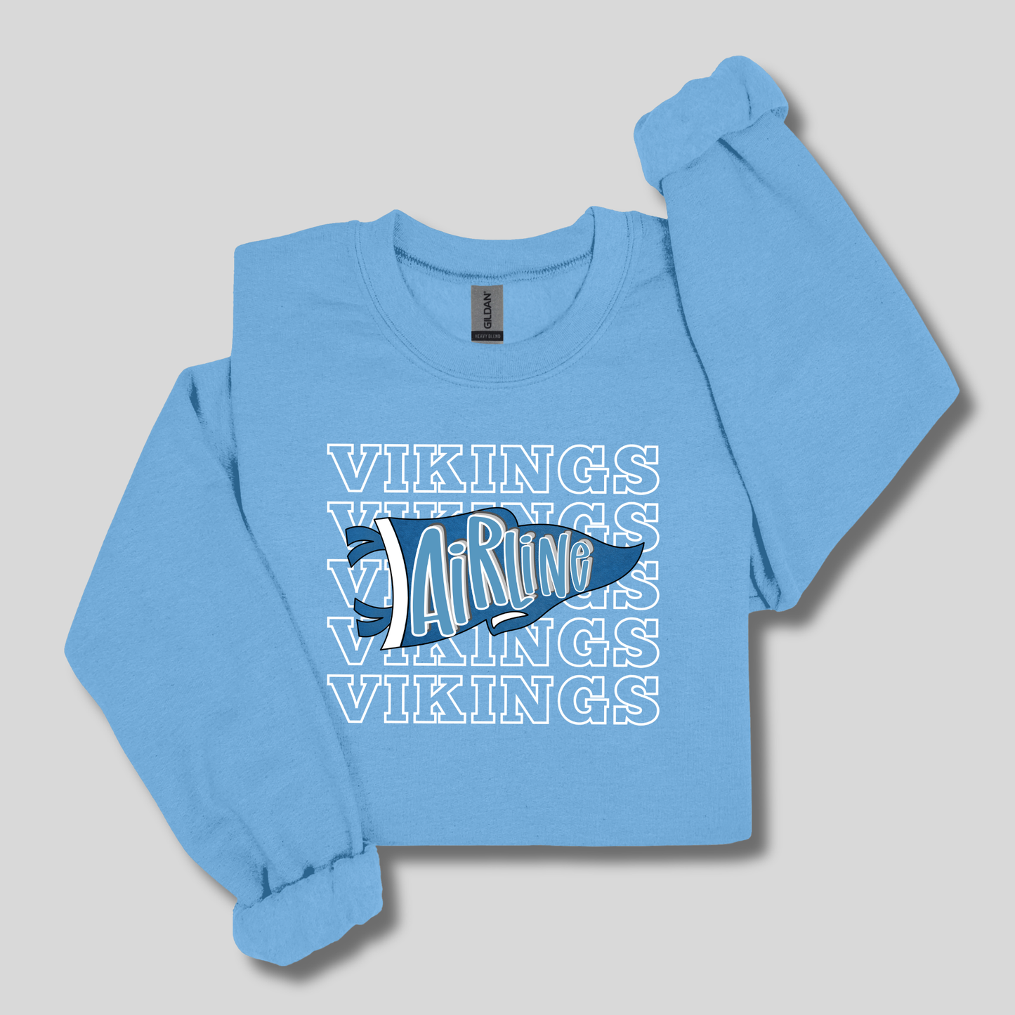 A light blue long-sleeve crewneck sweatshirt featuring a graphic print on the front with the word 'Vikings' repeated in white outline text and a blue Viking ship illustration.