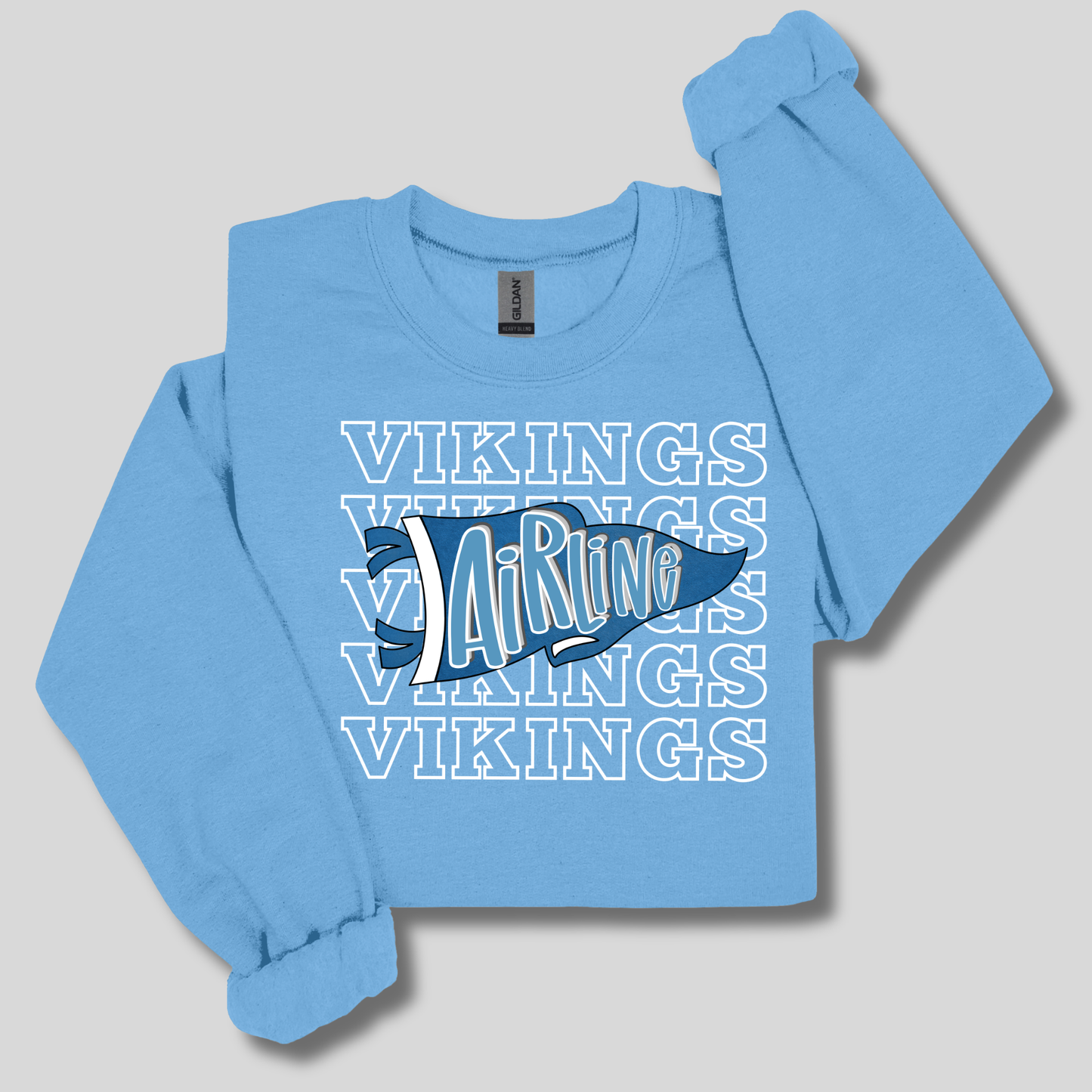 A light blue long-sleeve crewneck sweatshirt featuring a graphic design on the front with the word 'VIKINGS' repeated in white outline text and a dark blue and white hockey stick graphic in the center.