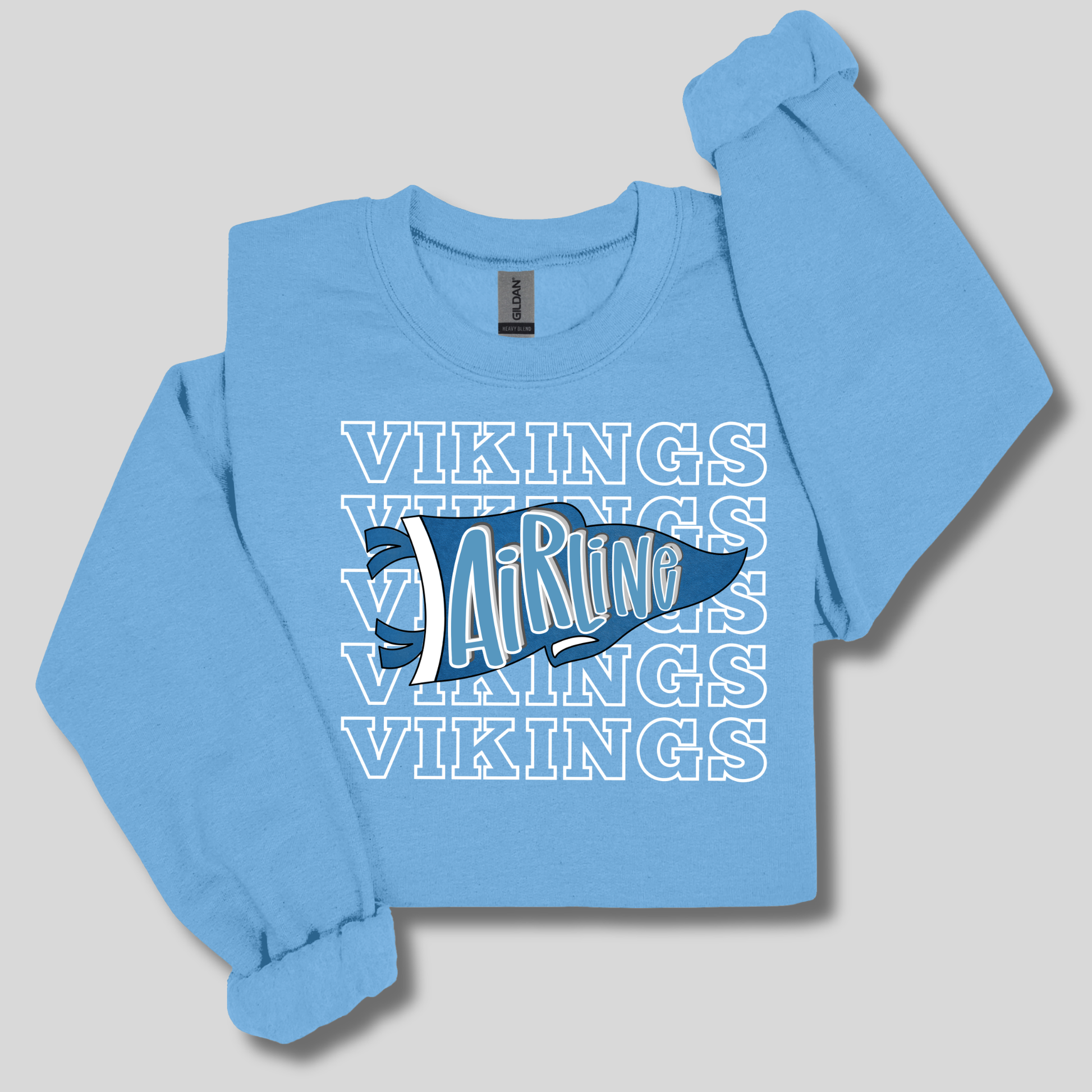A light blue long-sleeve crewneck sweatshirt featuring a graphic design on the front with the word 'VIKINGS' repeated in white outline text and a dark blue and white hockey stick graphic in the center.