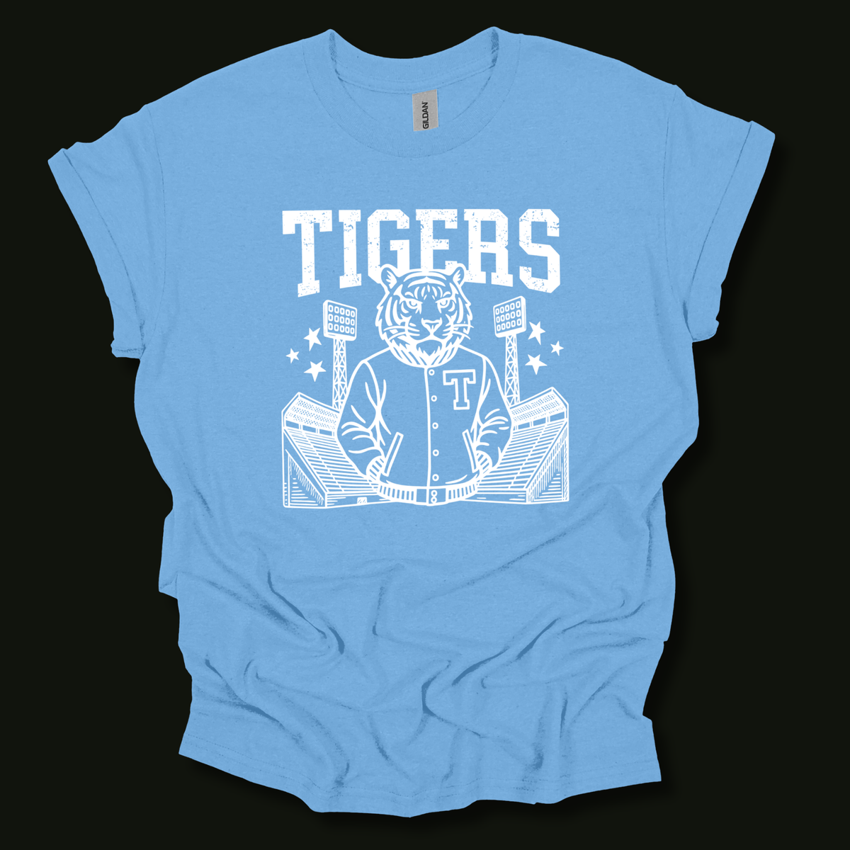 A light blue short-sleeve t-shirt with a white graphic print of a tiger mascot wearing a baseball jersey, holding a bat, with the word 'TIGERS' above, shown against a solid black background.