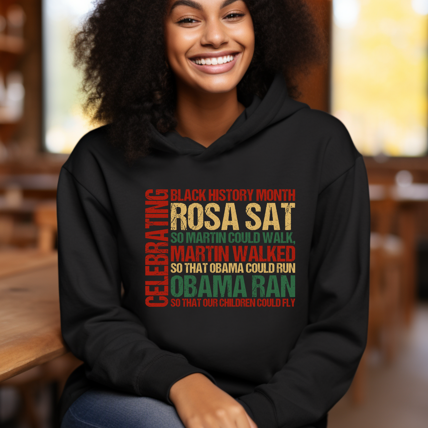 Person wearing a black hoodie with a colorful text design, sitting indoors.