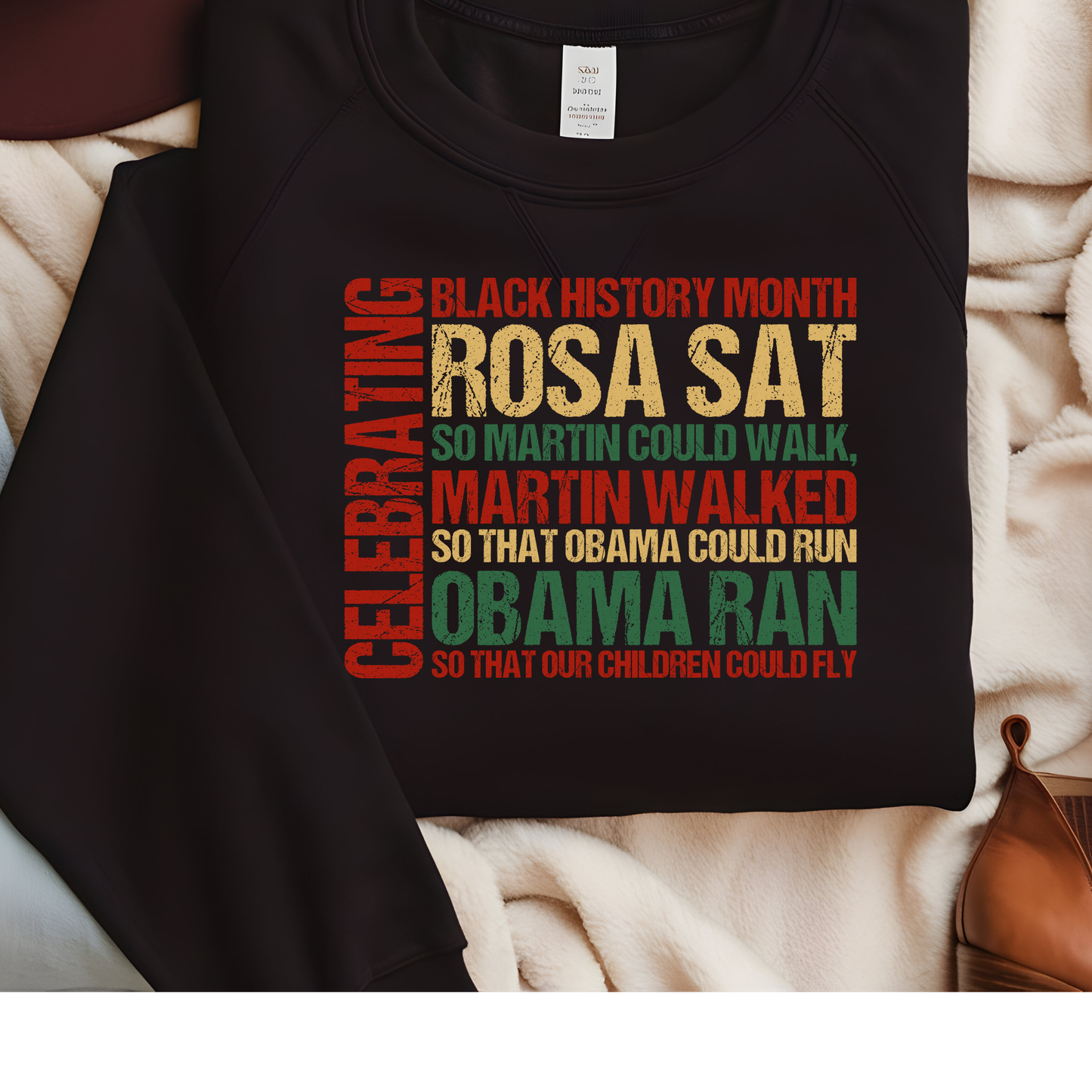 Black sweatshirt with colorful text celebrating Black History Month on a beige surface.