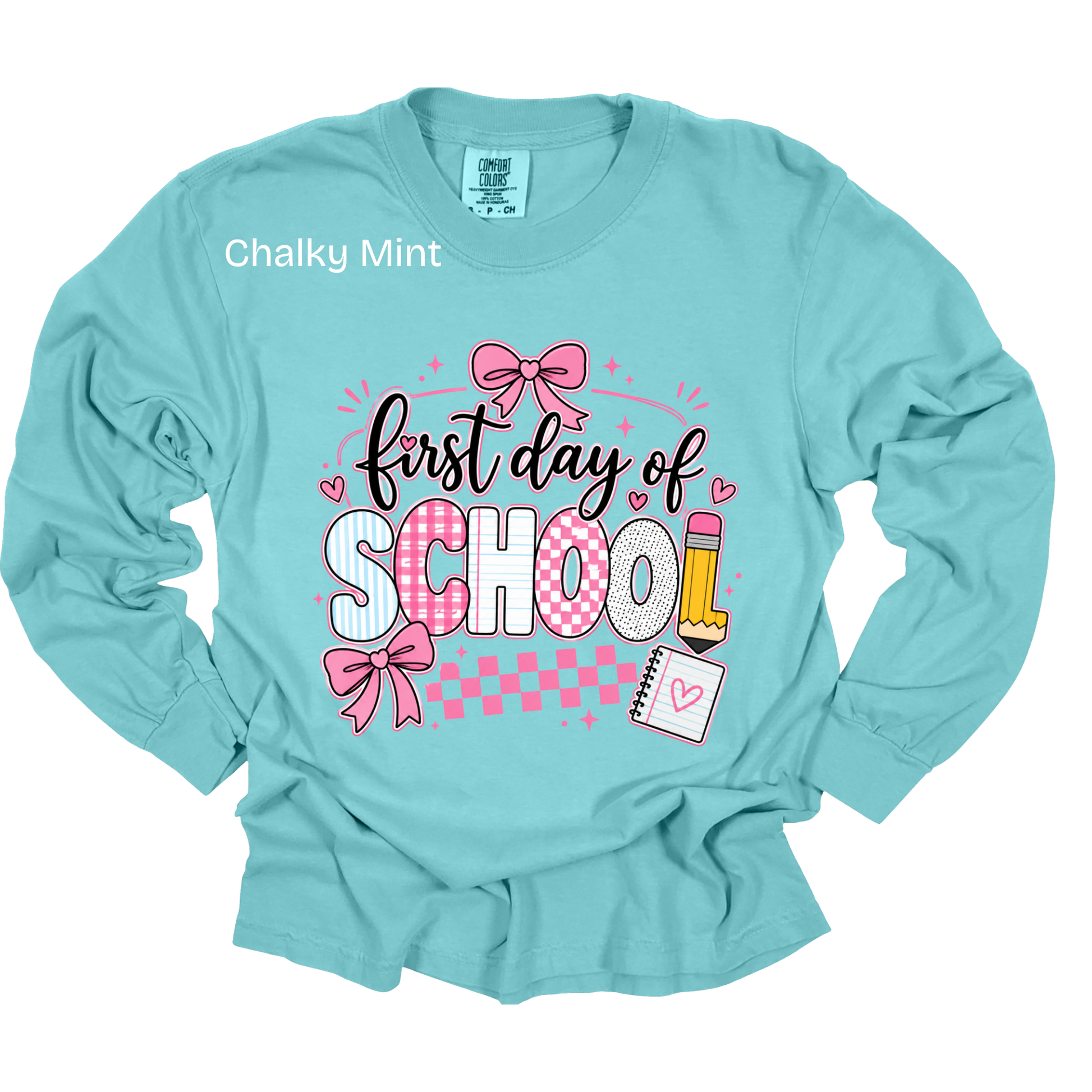 A long-sleeve crewneck t-shirt in a light aqua or 'Chalky Mint' color, featuring a 'first day of SCHOOL' graphic on the front with pink bows, checkered patterns, and school supplies.