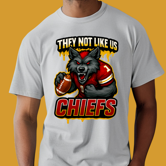 Person wearing a t-shirt with a graphic of a wolf holding a football and text 'They Not Like Us Chiefs' on a yellow background. Chiefs Mascot Shirt - Chiefs They Not Like Us Football Game Day Tee
