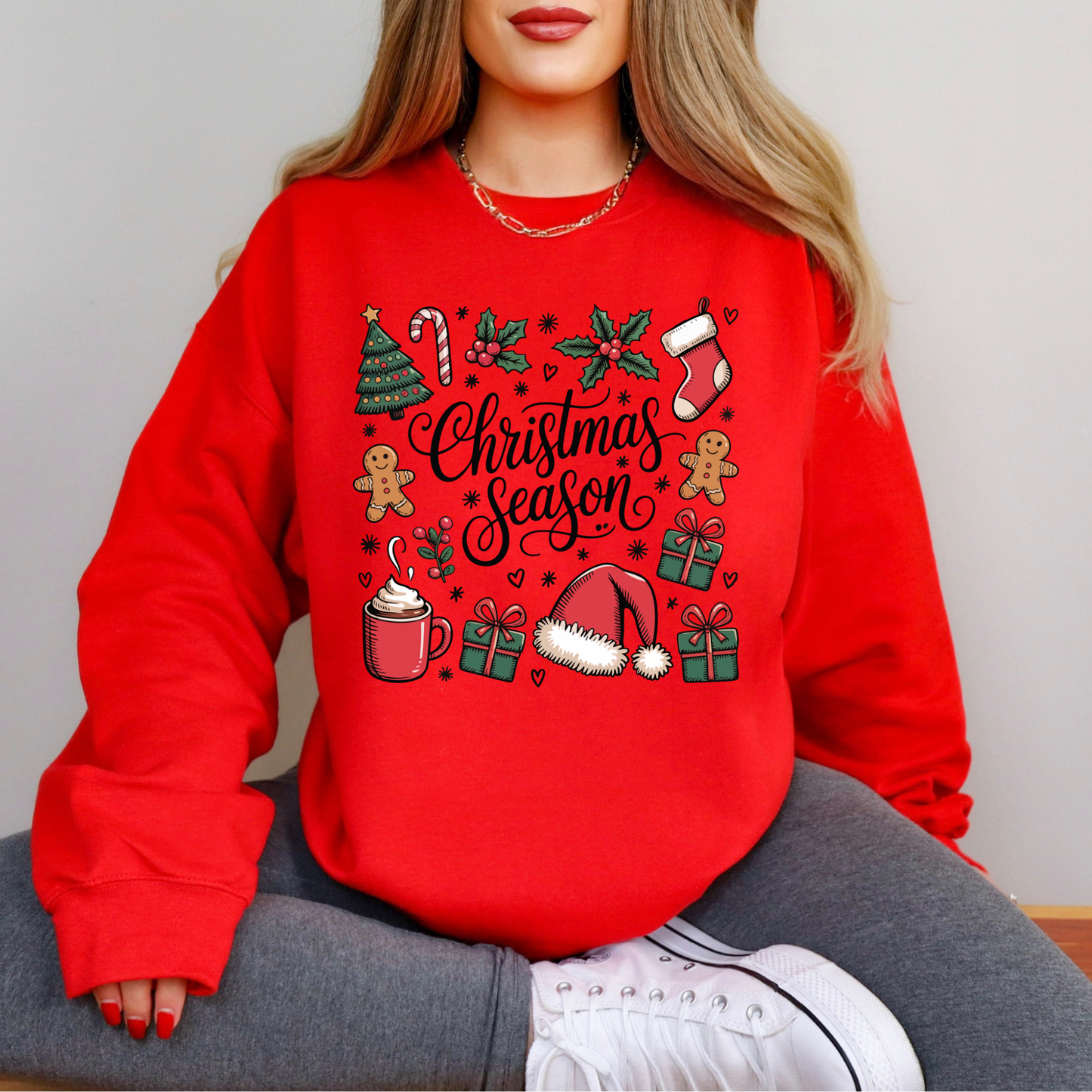 Red sweatshirt with Christmas-themed design worn by a person sitting on a chair.