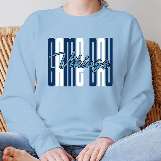A person wearing a light blue sweatshirt with a 'GAME DAY Vikings' graphic on the chest, seated in a wicker chair.