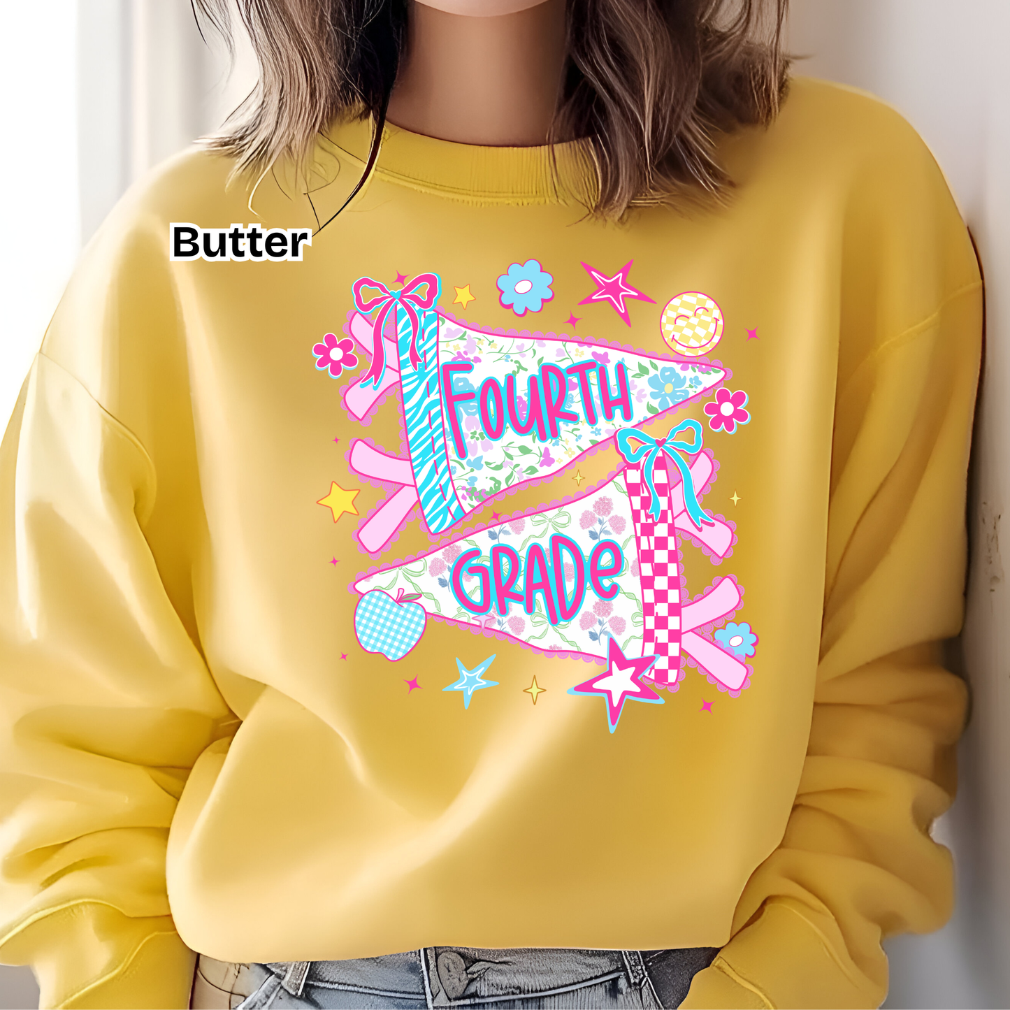 A person wearing a yellow sweatshirt with a colorful 'FOURTH GRADE' pennant graphic on the chest, paired with blue jeans. The word 'Butter' is printed on the upper left chest area.