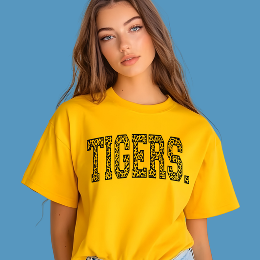 Woman wearing a yellow 'TIGERS' t-shirt against a blue background Custom Mascot Shirt - Tigers Leopard Varsity Typography Game Day T-Shirt