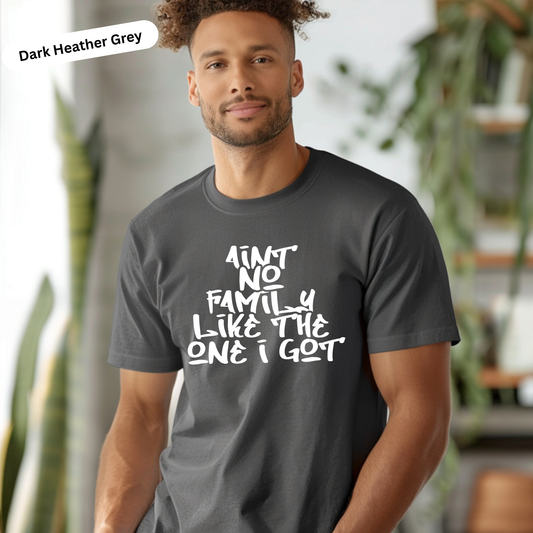 Man wearing a dark Heather Grey t-shirt with text, standing indoors with plants in the background.