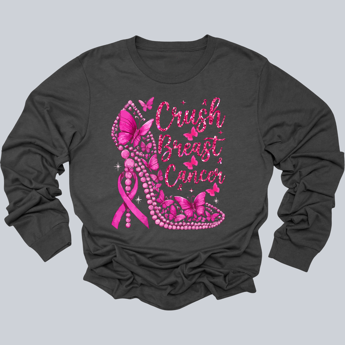A dark charcoal gray long-sleeve t-shirt with a graphic on the front featuring a pink breast cancer awareness ribbon, butterflies, pearls, and the text 'Crush Breast Cancer' in pink glitter-style lettering, shown on a solid gray background.