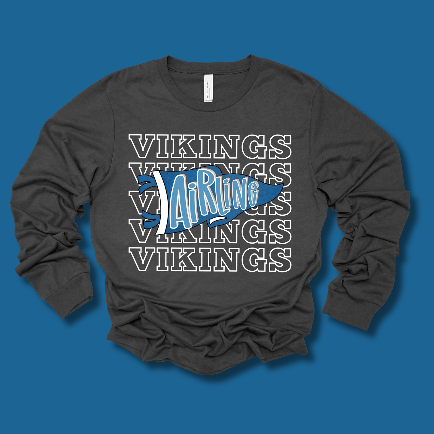 A dark charcoal gray long-sleeve t-shirt with a graphic design on the front, laid flat against a solid purple background. The graphic features the word 'BENTON' repeated in white outline letters, overlaid with a purple and pink stylized 'Tigers' logo with yellow accents.