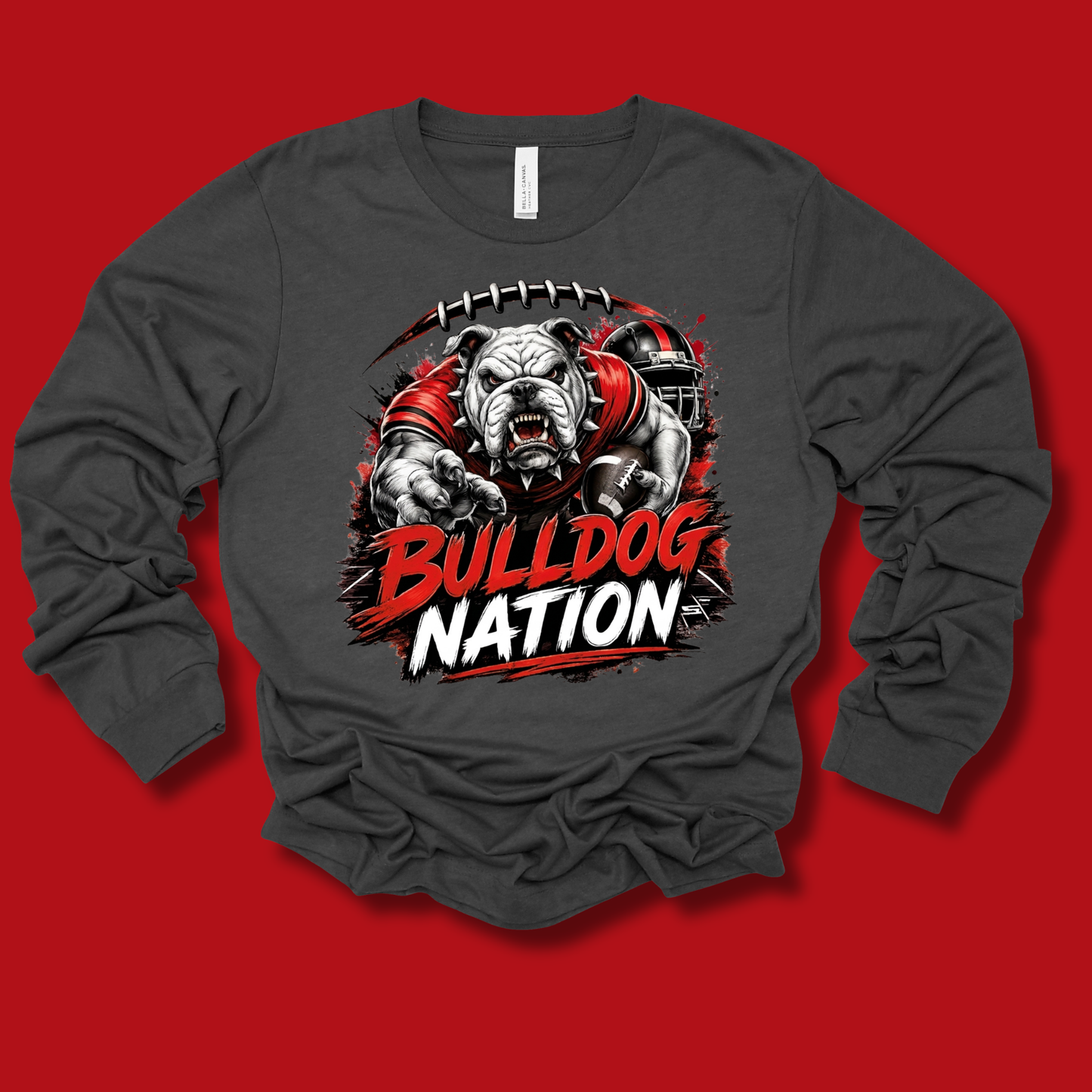 A dark gray long-sleeve t-shirt with a graphic of a bulldog mascot wearing a red jersey, with the text 'BULLDOG NATION' in red and white. The shirt is displayed flat against a solid red background.