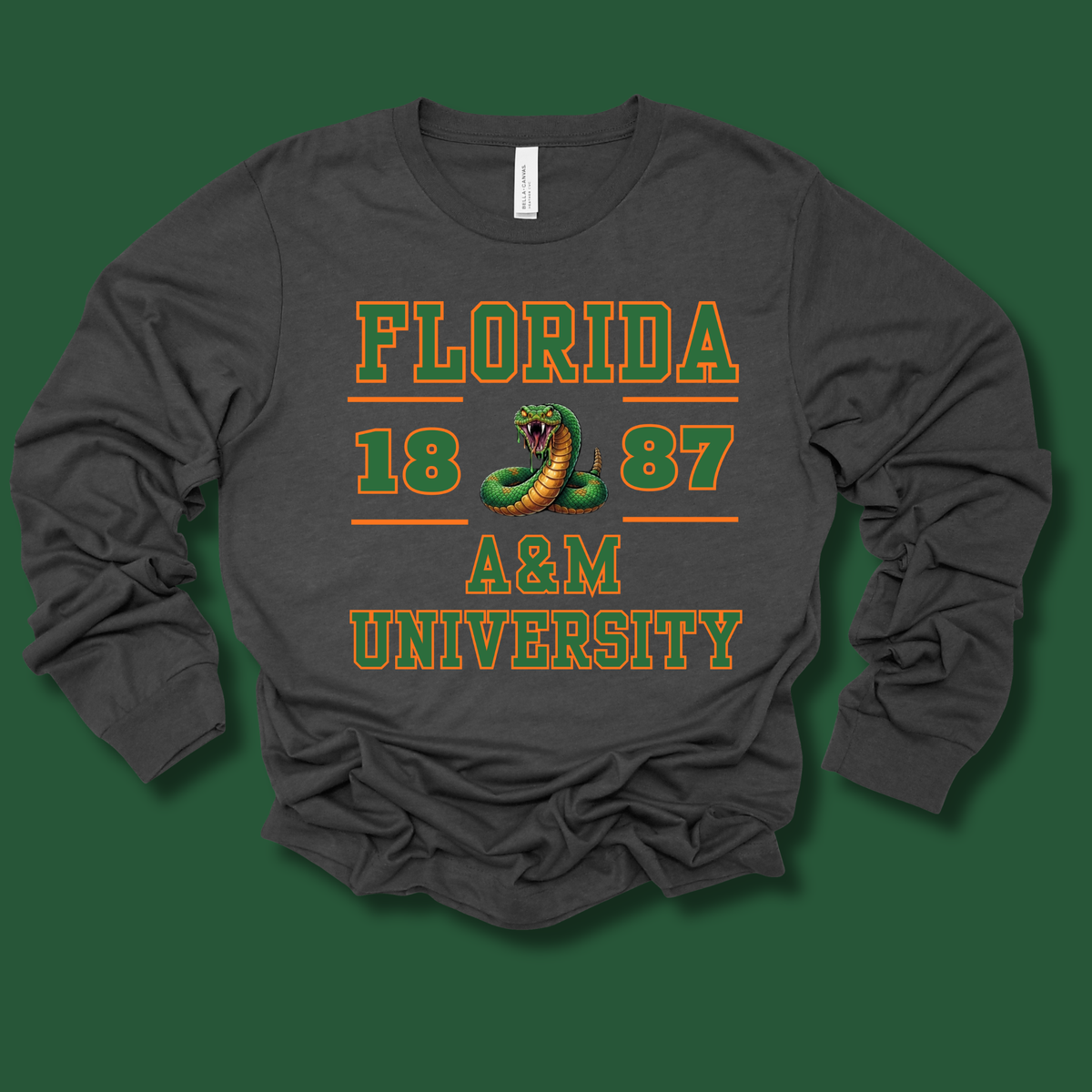 A dark gray long-sleeve t-shirt with a vintage-style graphic on the front reading 'FLORIDA 1887 A&M UNIVERSITY' in green and yellow, featuring a coiled green snake in the center, laid flat on a solid dark green background.