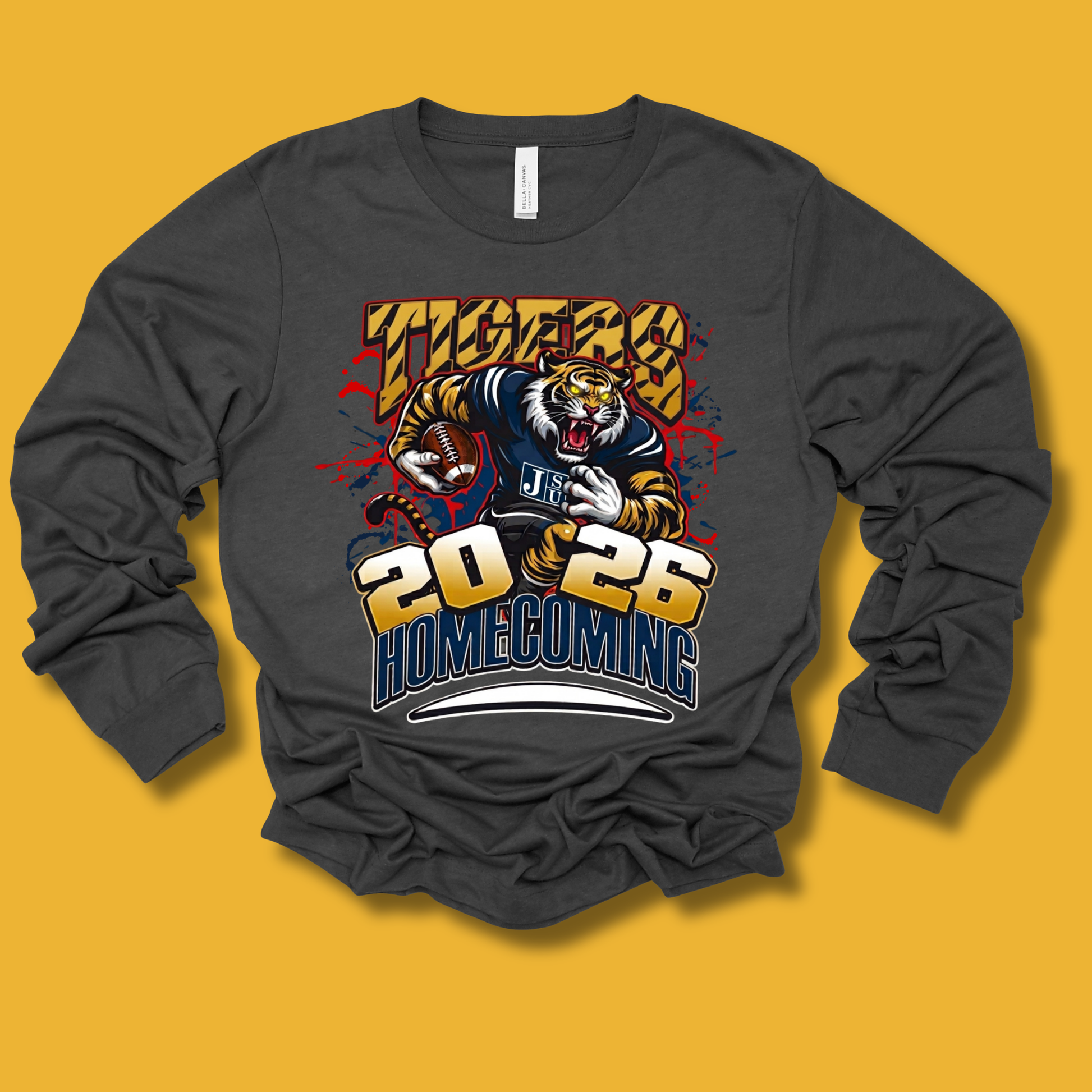 A dark gray long-sleeve t-shirt with a graphic print of a tiger football player and the text 'TIGERS 2026 HOMECOMING', displayed on a solid yellow background.