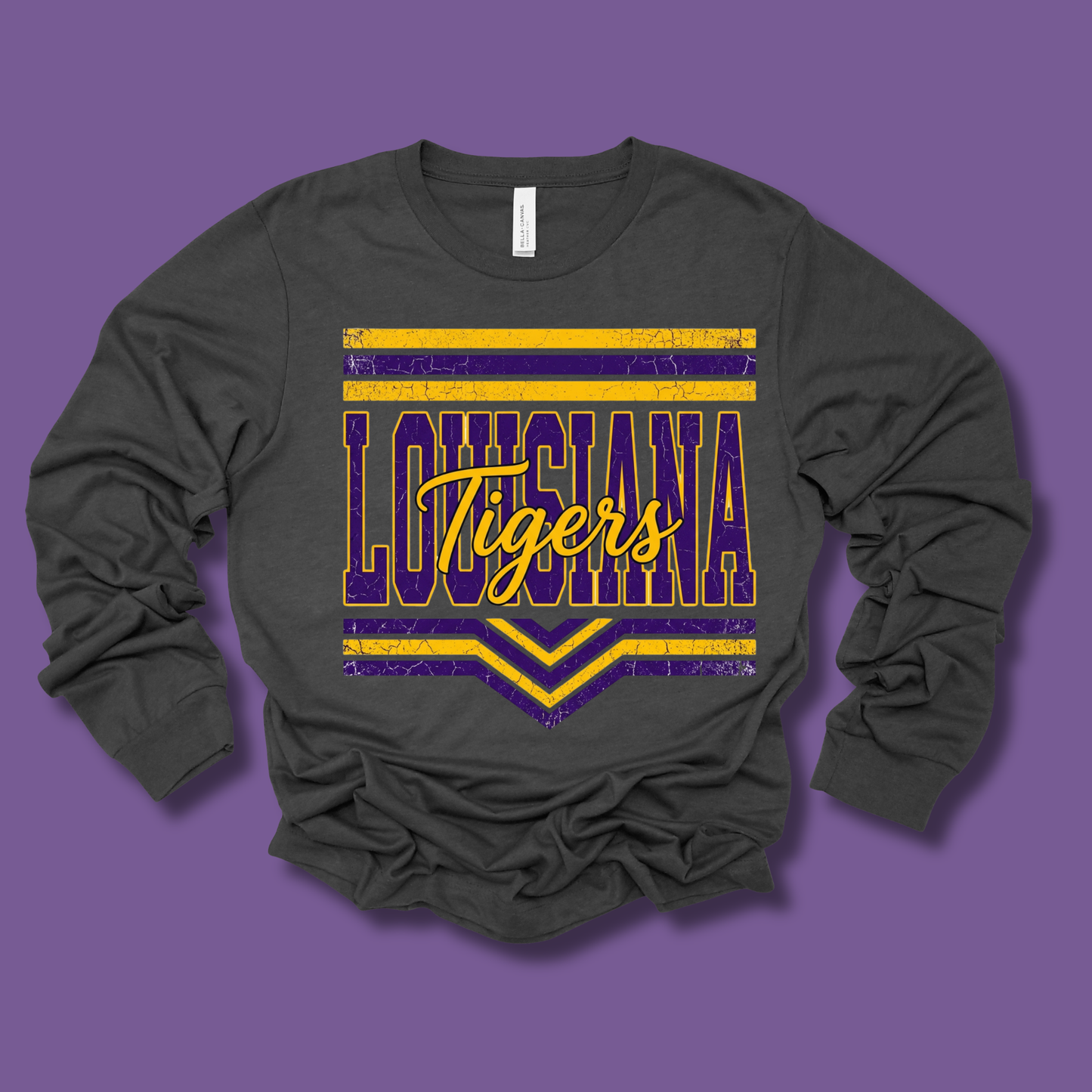 A dark charcoal gray long-sleeve t-shirt with a distressed purple and yellow graphic reading 'LOUISIANA Tigers' on the front, displayed against a solid purple background.