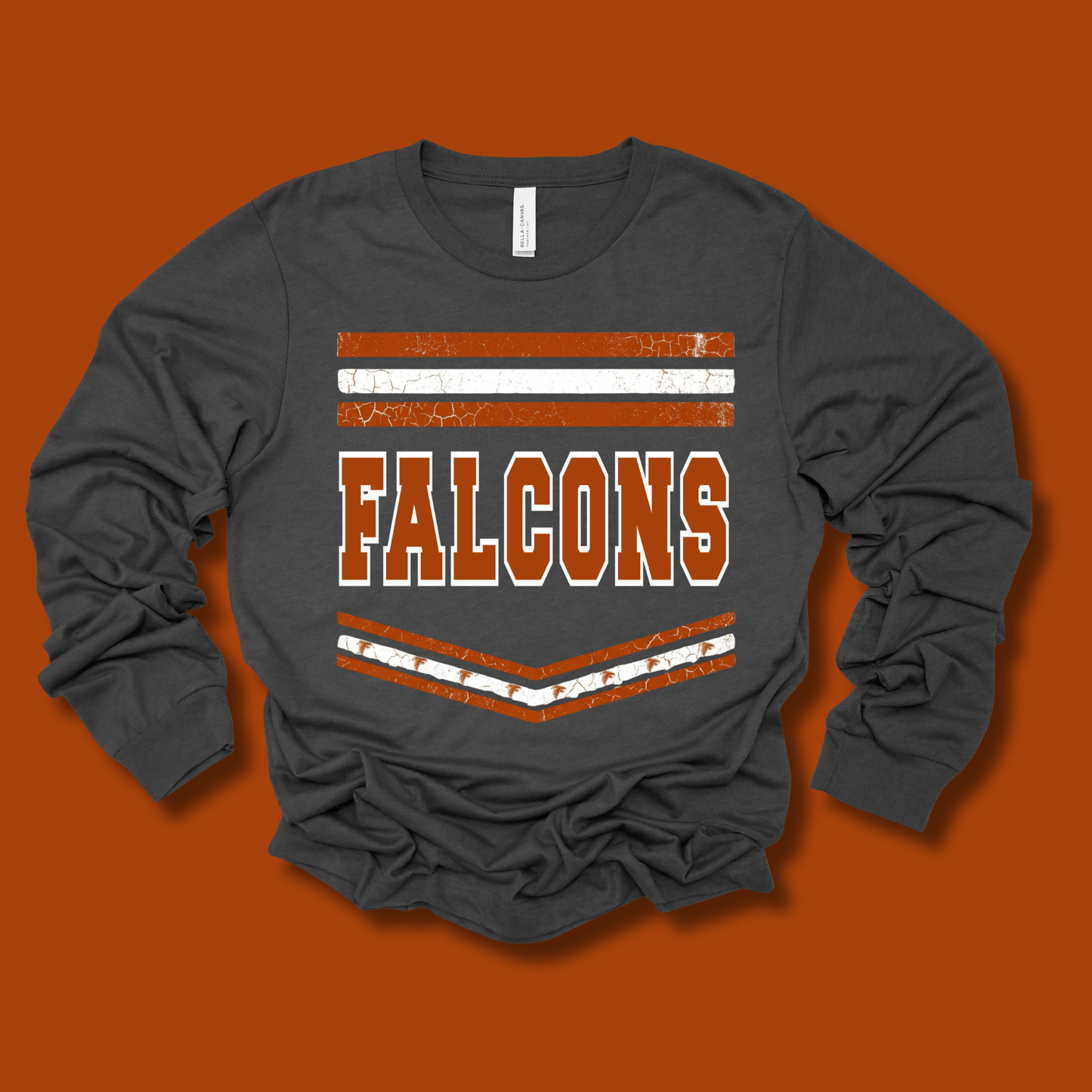 A dark gray long-sleeve t-shirt with a distressed orange and white graphic reading 'FALCONS' on the front, laid flat against a solid orange background.