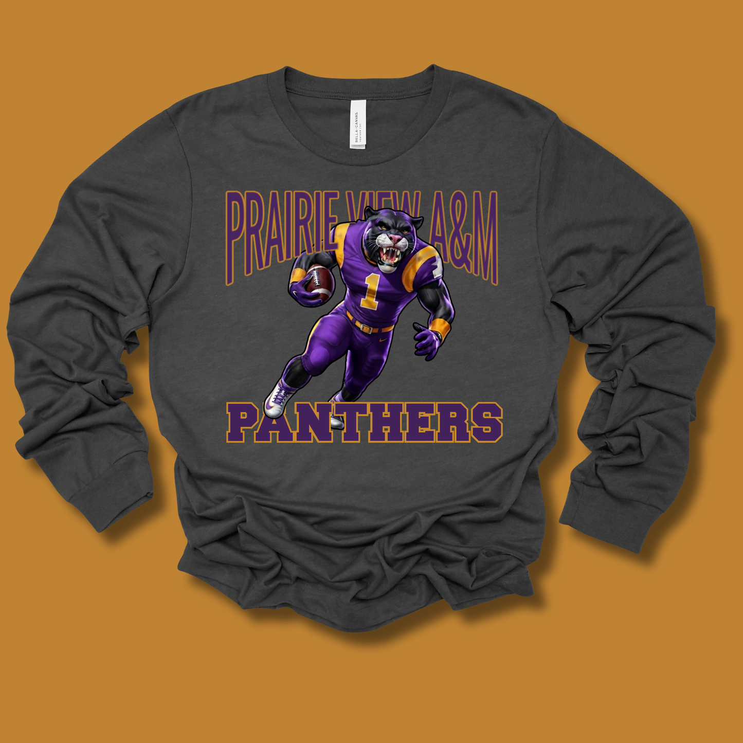 A dark charcoal gray long-sleeve t-shirt with a graphic of a purple and gold football player and the text 'PRAIRIE VIEW A&M PANTHERS' on the front, displayed against a solid orange-brown background.