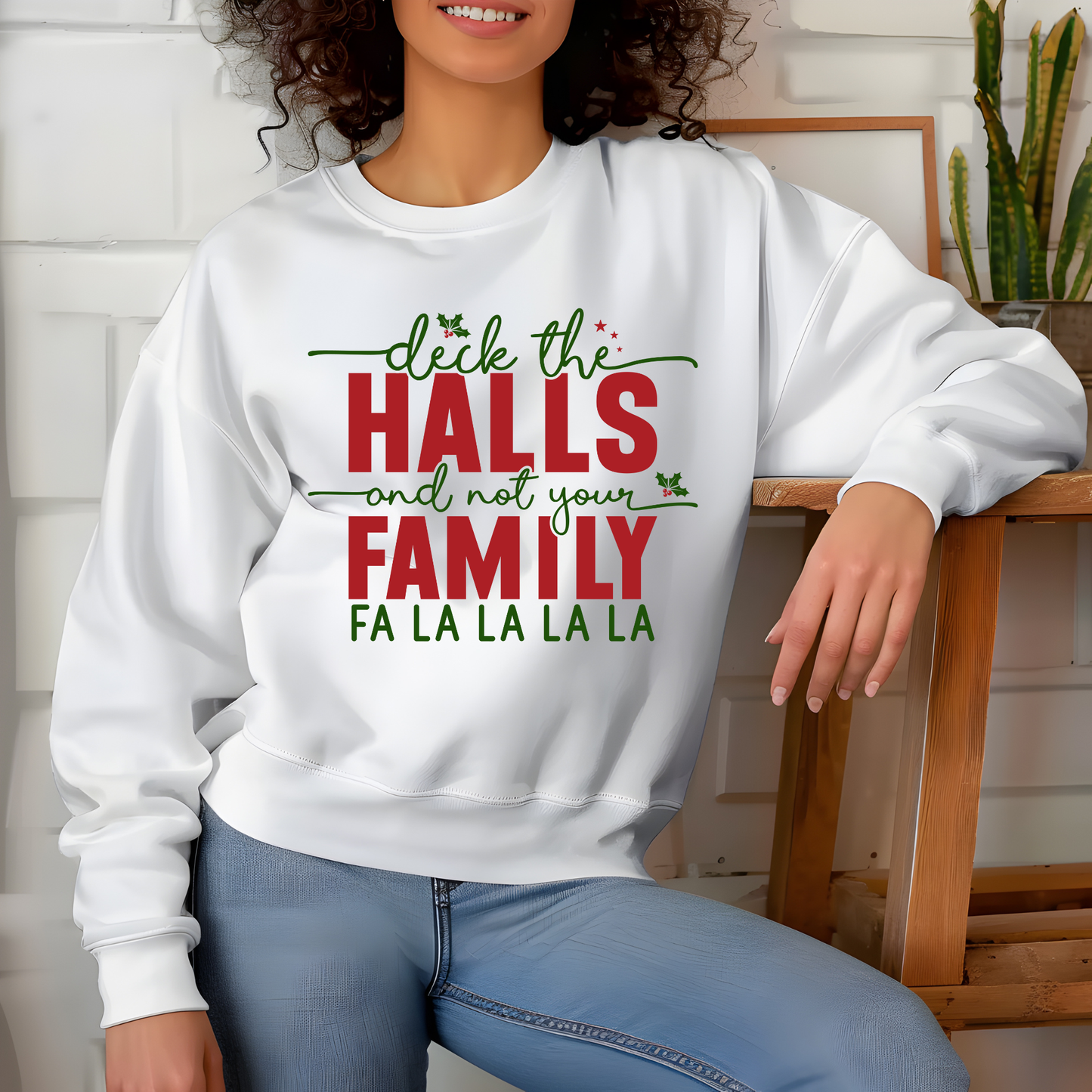 Person wearing a white sweatshirt with Christmas-themed text, sitting on a wooden chair.