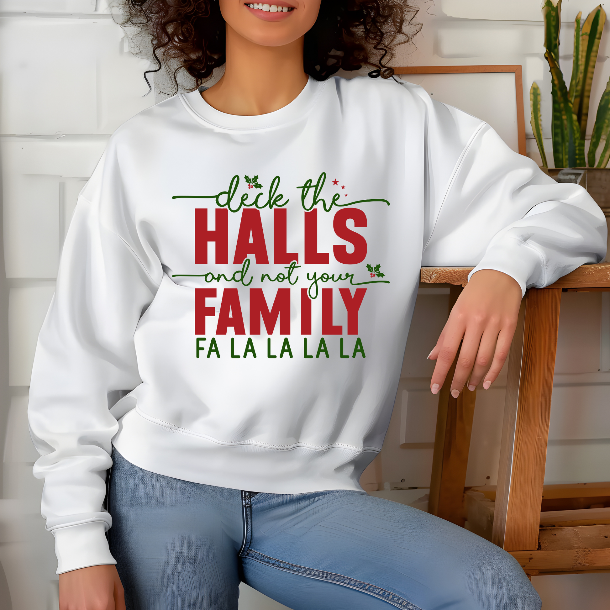 Person wearing a white sweatshirt with Christmas-themed text, sitting on a wooden chair.