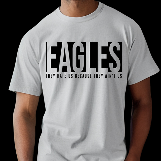 White t-shirt with 'EAGLES THEY HATE US BECAUSE THEY AIN'T US' text on a black background Eagles School Mascot Shirt - Eagles Game Day Cool School Spirit Tee