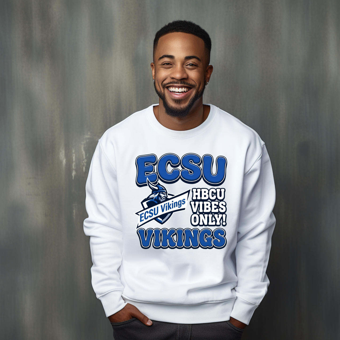 A smiling man wearing a white crewneck sweatshirt with a blue and white ECSU Vikings graphic, standing against a textured gray background.