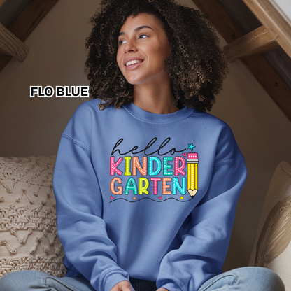 A woman wearing a light blue sweatshirt with a colorful 'hello KINDER GARTEN' graphic, sitting in a cozy indoor setting. The text 'FLO BLUE' is displayed on the left side.