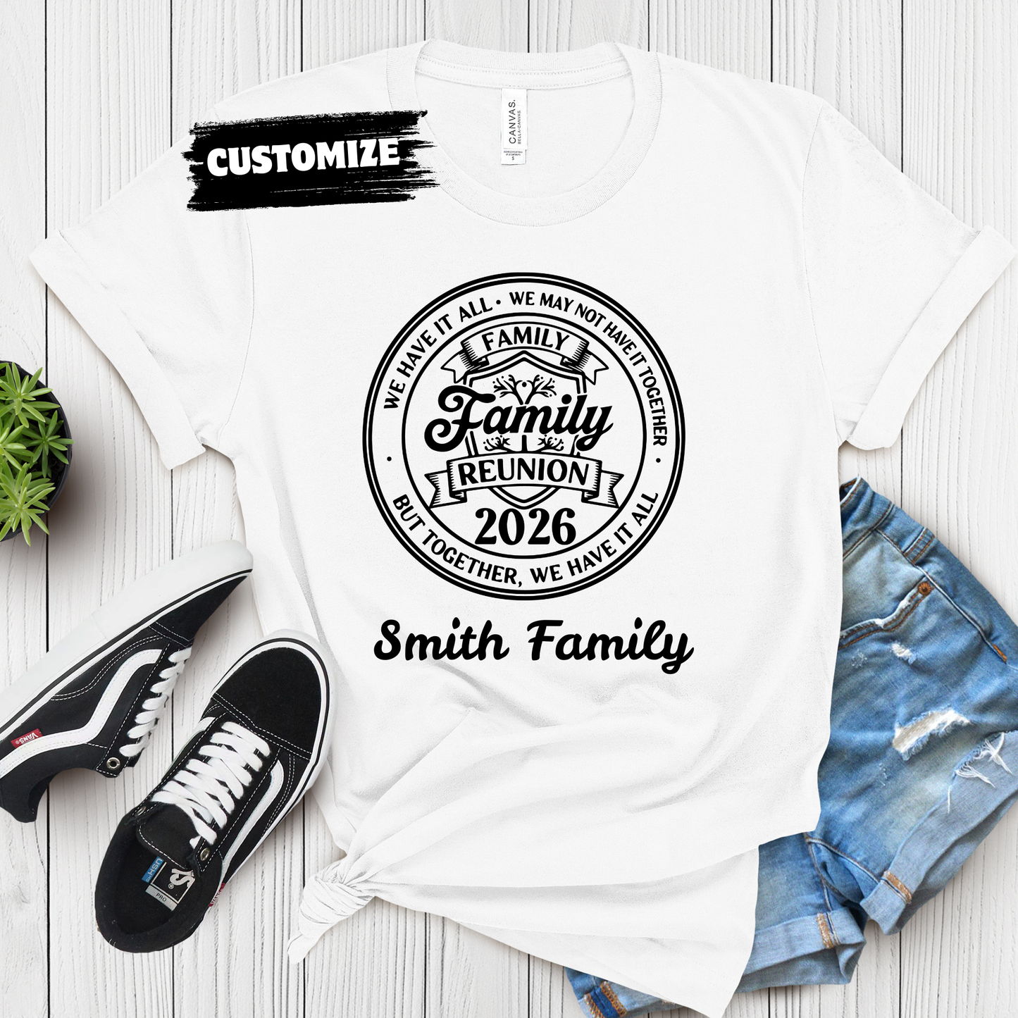 White t-shirt with 'Family Reunion 2026' design, shoes, and jeans on a wooden surface.