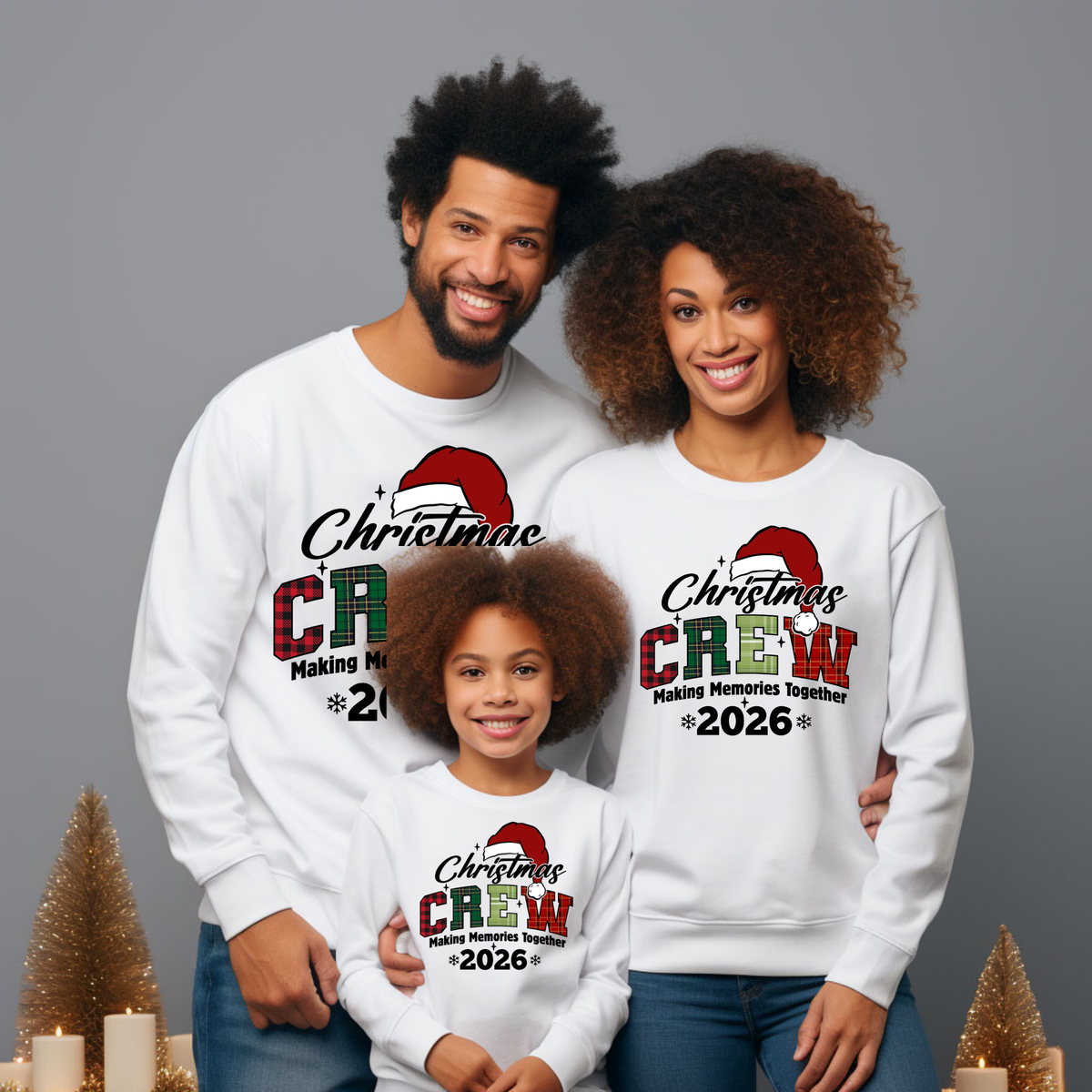 A family of four wearing matching white crewneck sweatshirts with a 'Christmas CREW Making Memories Together 2026' graphic, posed against a solid gray studio background with decorative gold trees.