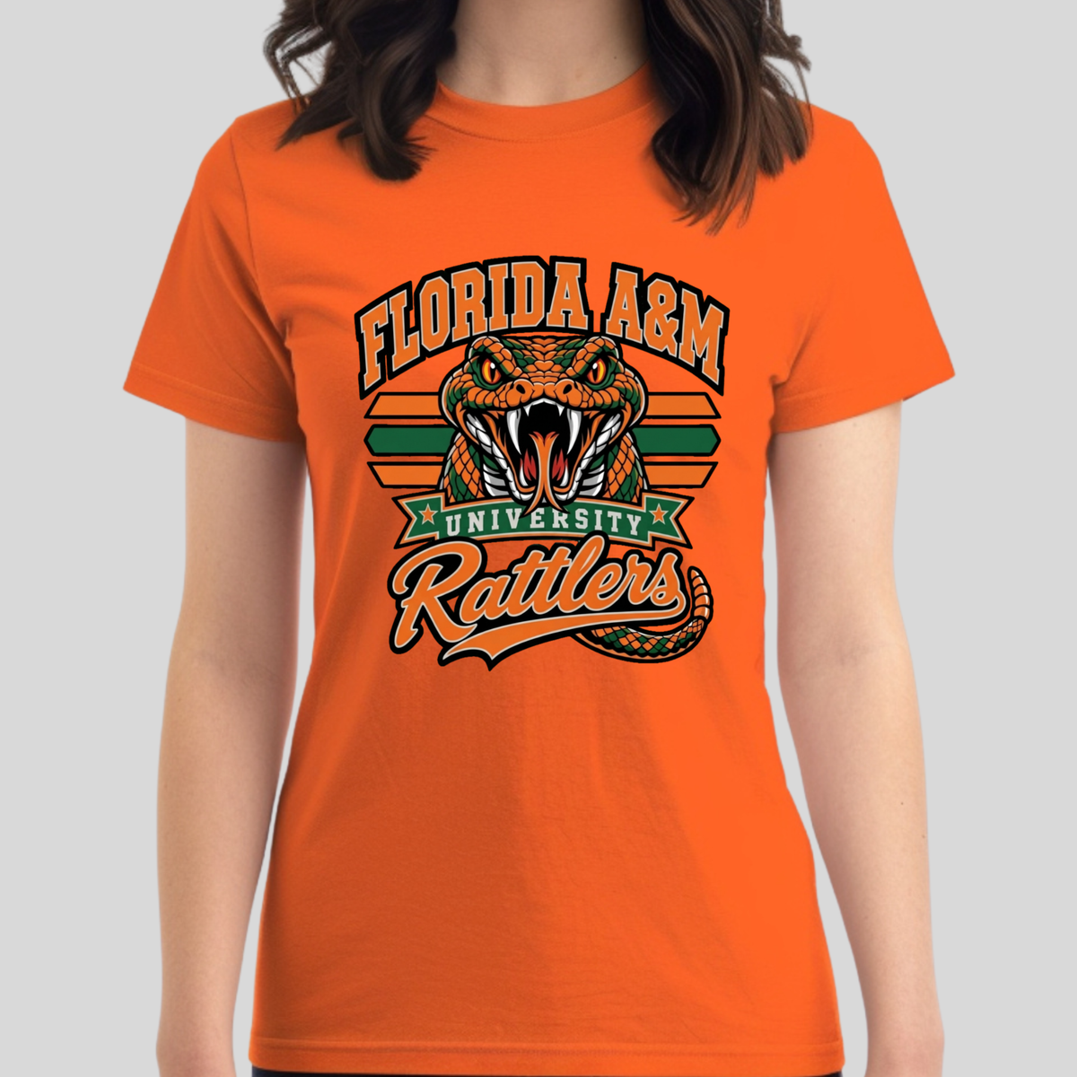 A woman wearing a bright orange short-sleeve t-shirt with a retro-style Florida A&M University Rattlers graphic on the front, set against a solid light gray background.