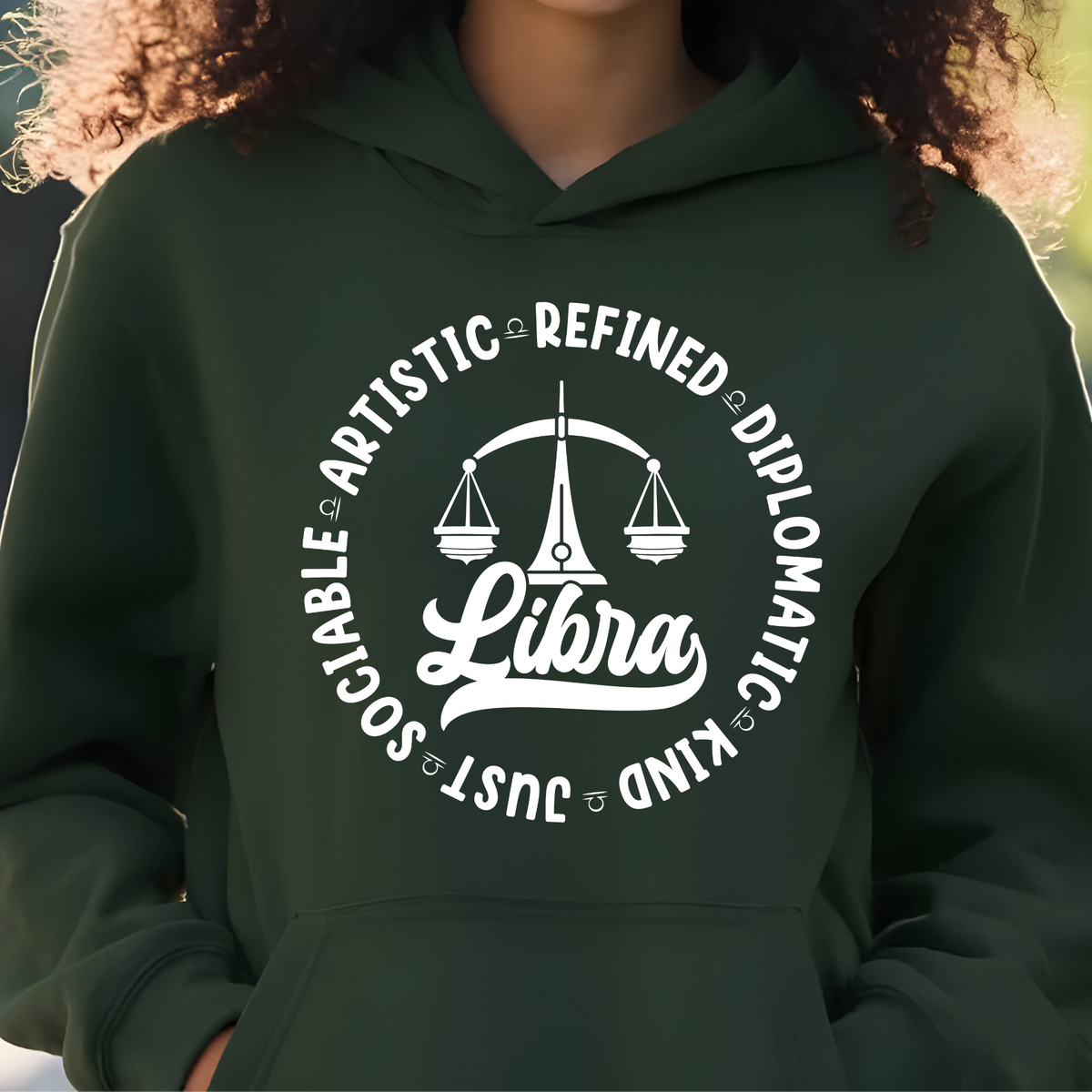 A person wearing a dark green hoodie with a white circular graphic on the chest featuring a scale of justice and the word 'Libra' surrounded by adjectives like diplomatic, refined, and social.