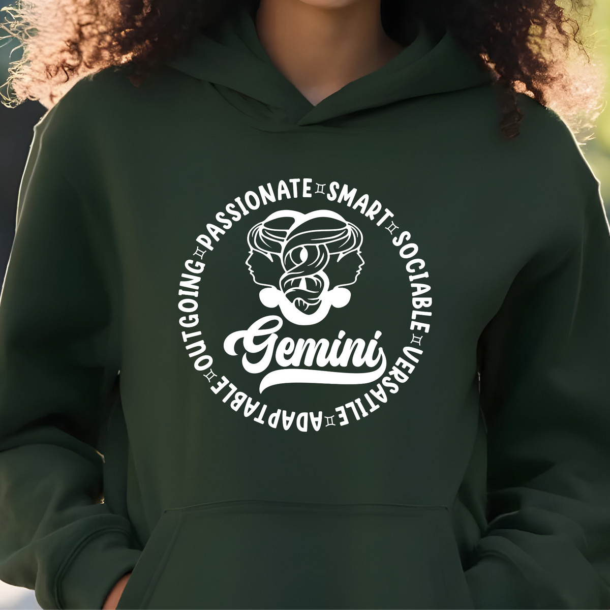 A person wearing a dark green hoodie with a white circular Gemini graphic on the chest, photographed from the neck down against a softly blurred outdoor background.