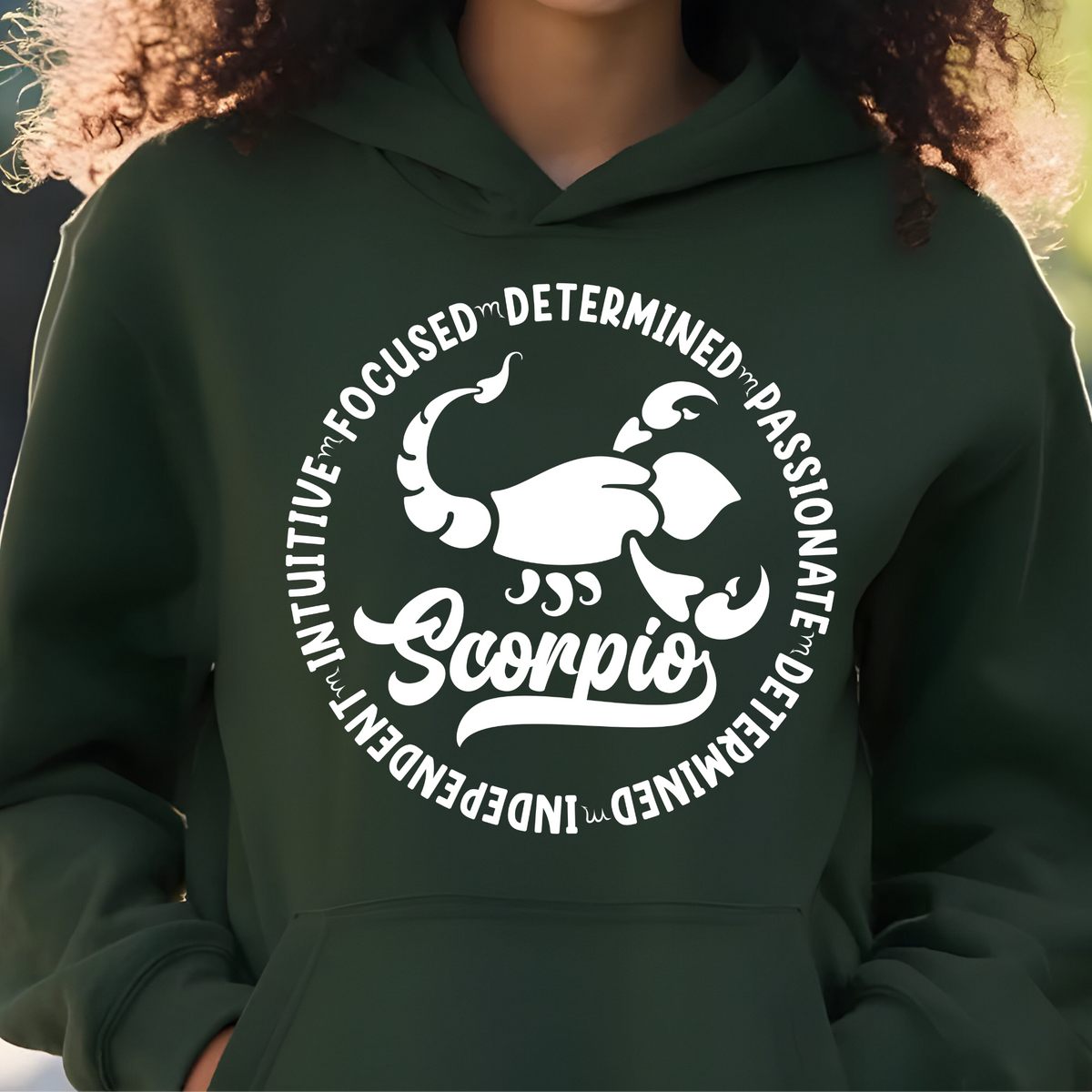 Woman wearing a black crewneck sweatshirt featuring a white circular Scorpio zodiac graphic with a scorpion illustration, the word "Scorpio," and trait keywords like intuitive, focused, determined, passionate, and independent.