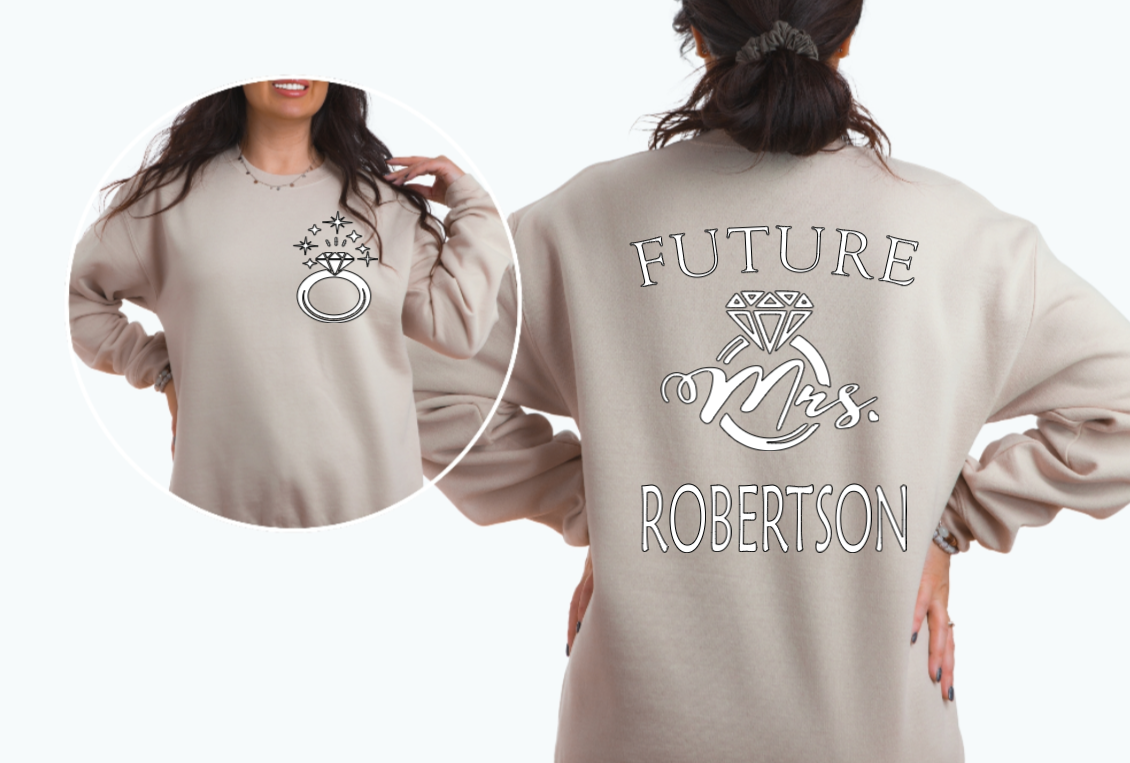 Woman wearing sand sweater with FUTURE Mrs. on the back with bling ring on the front indicating engagement announcement shirt for bridal shower or engagement party and gift for new bride to be. 