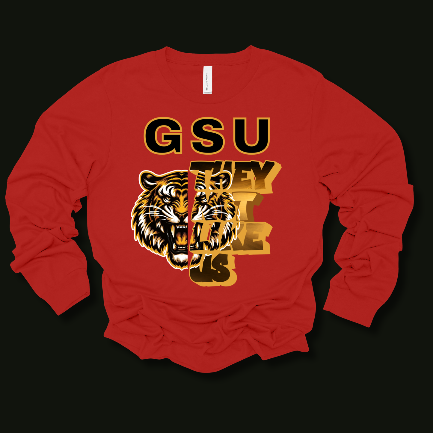 A red long-sleeve t-shirt with a graphic print featuring a tiger head and the text 'GSU THEY CAN'T BELIEVE US' in black and gold, displayed on a solid black background.