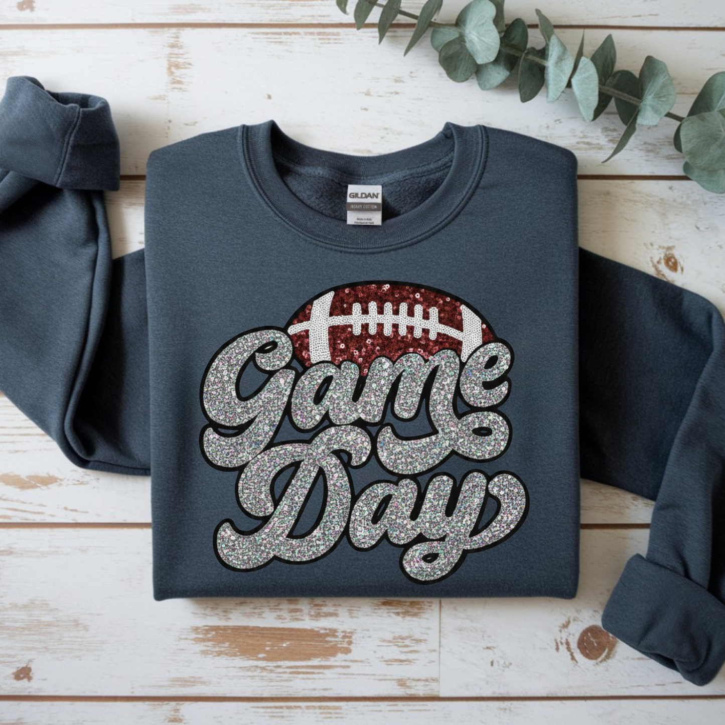 Dark blue sweatshirt with 'Game Day' text and football graphic on a wooden surface.