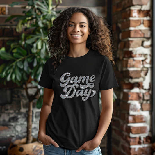 Woman wearing a black 'Game Day' t-shirt standing in front of a brick wall.