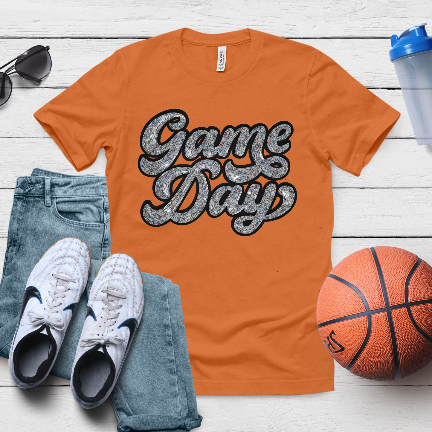 Orange 'Game Day' t-shirt with jeans, sneakers, and a basketball on a wooden surface.